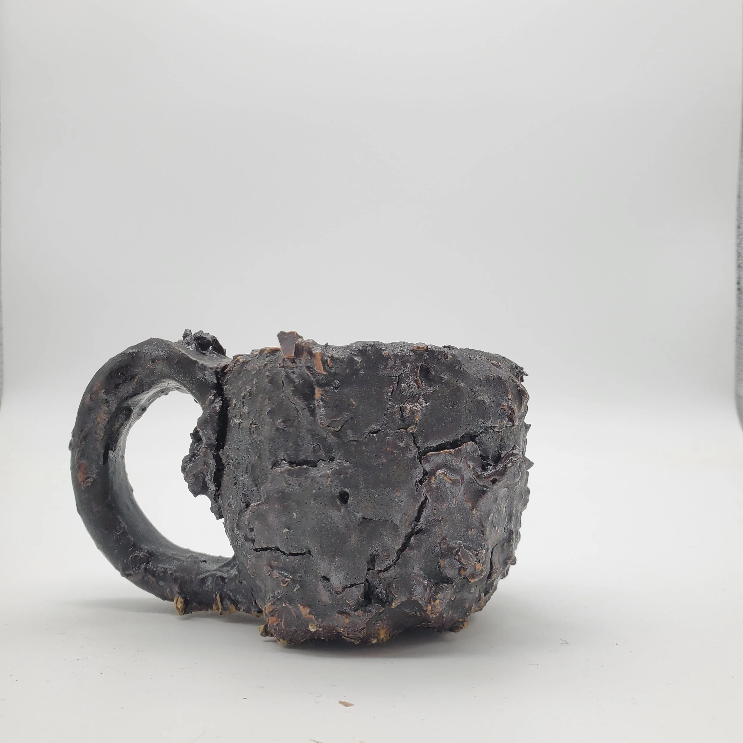 Charred, broken ceramic mug with a blackened, cracked surface on a plain white background.