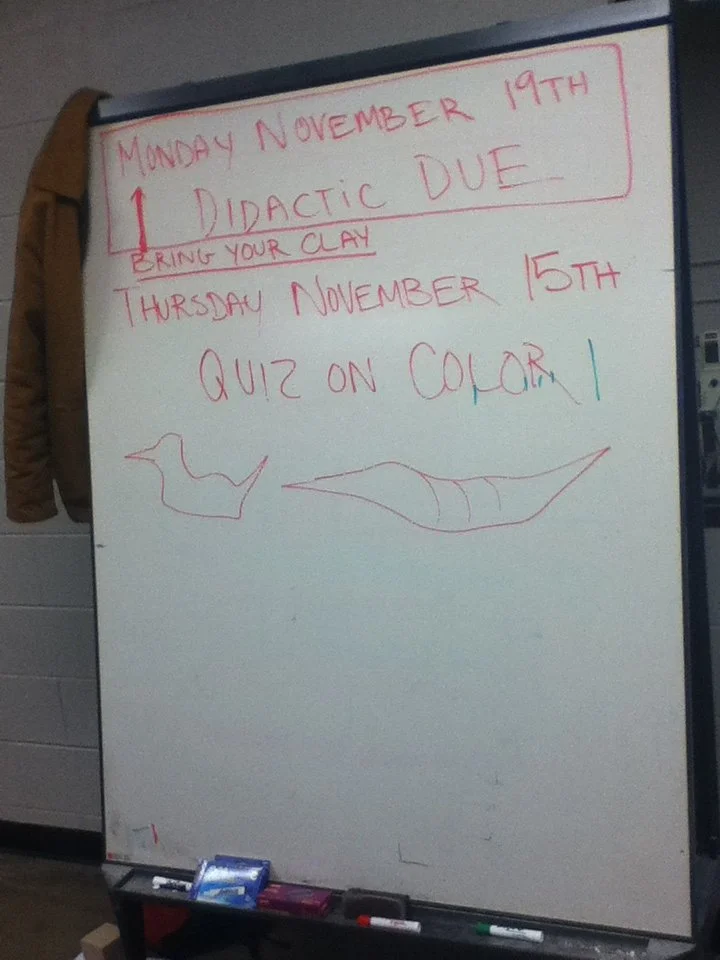 Whiteboard with red and blue writing announcing important dates for November, including a didactic due date on November 19th and a quiz on color on November 15th, with doodles of a bird and a fish.