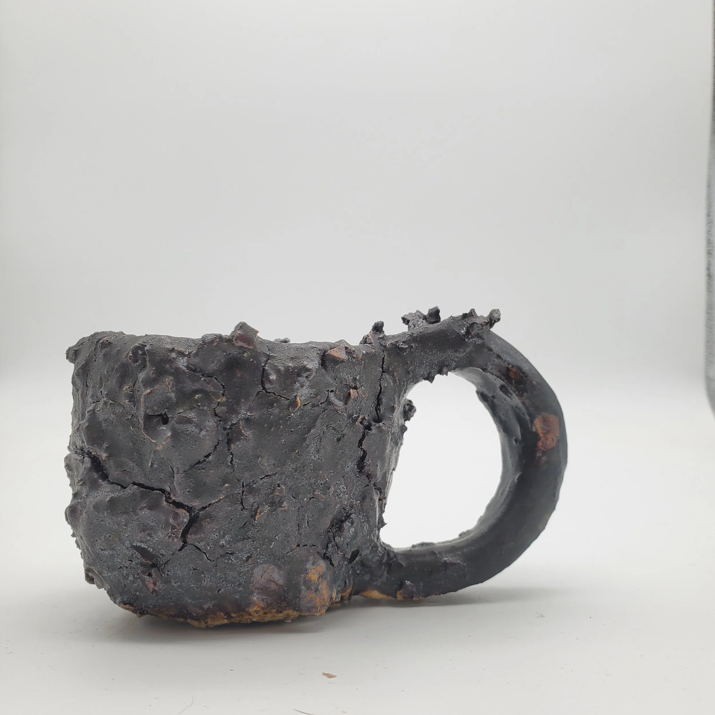 A burnt, blackened mug with a cracked and charred surface, showing signs of significant fire damage, against a plain white background.