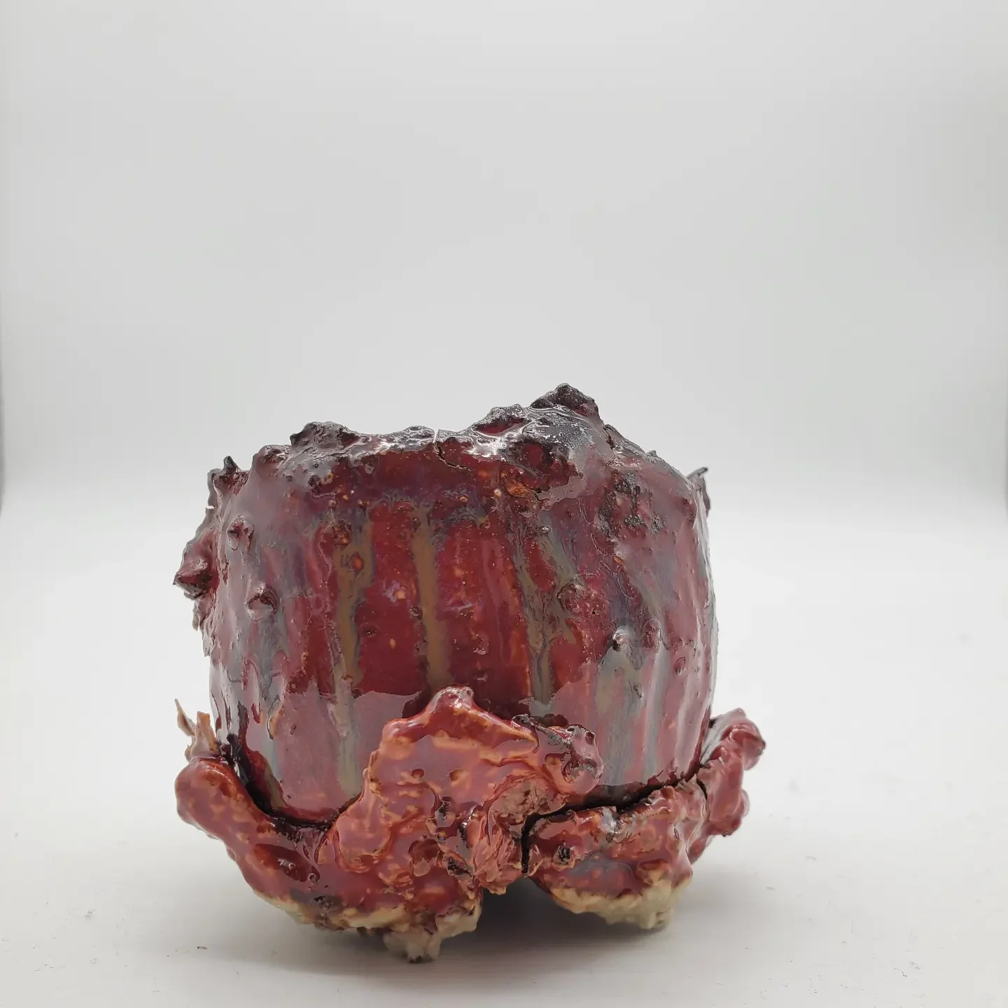 A burnt, irregularly shaped apple with blackened and shriveled skin, placed on a plain white surface.