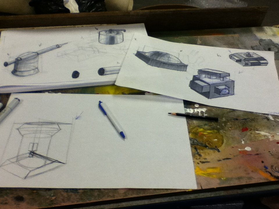 Sketches of various objects including a boat, a camera, and containers on sheets of paper, with drawing tools on a cluttered work table.