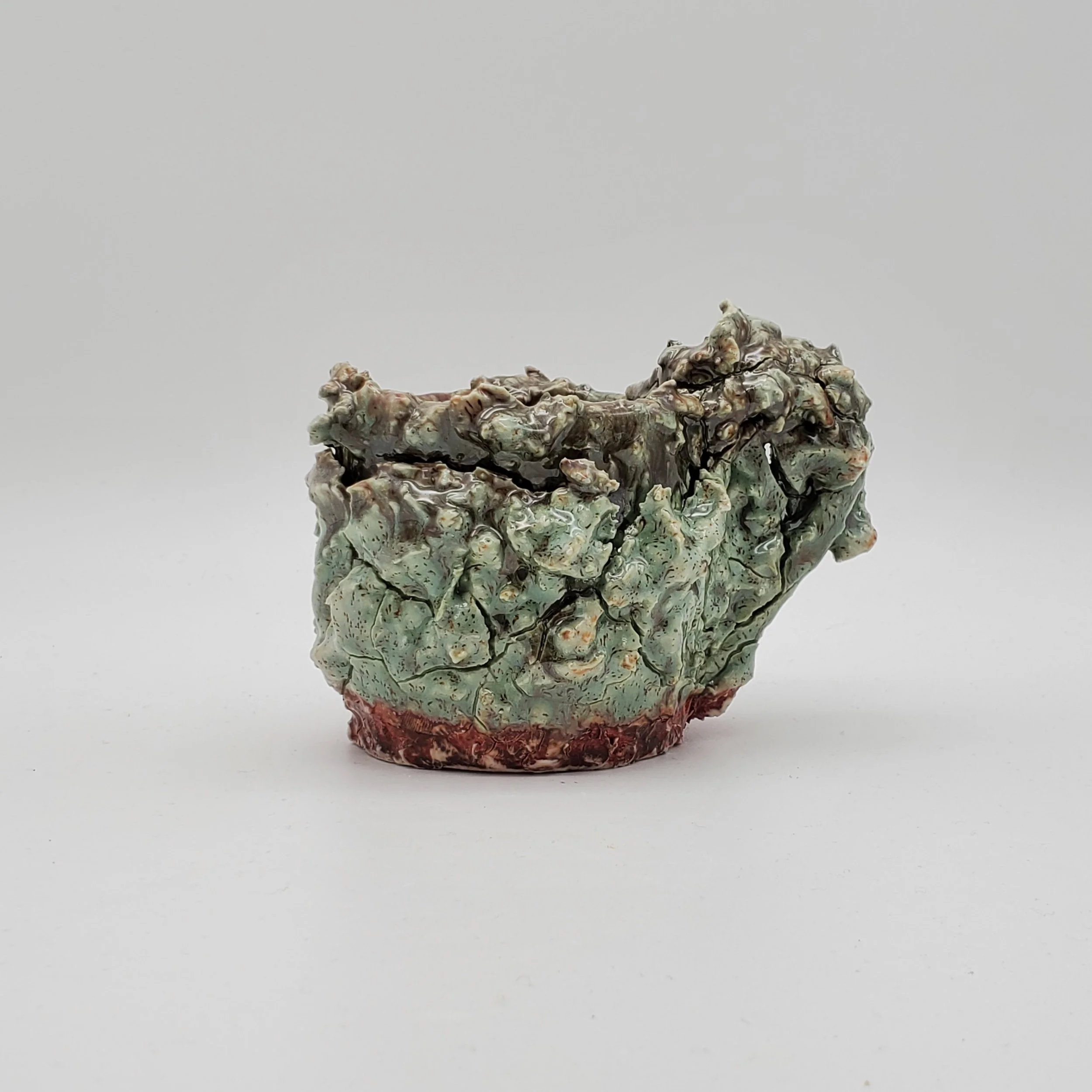 Ceramic bowl with a textured, crackled glaze in green and brown colors, placed on a plain white surface.