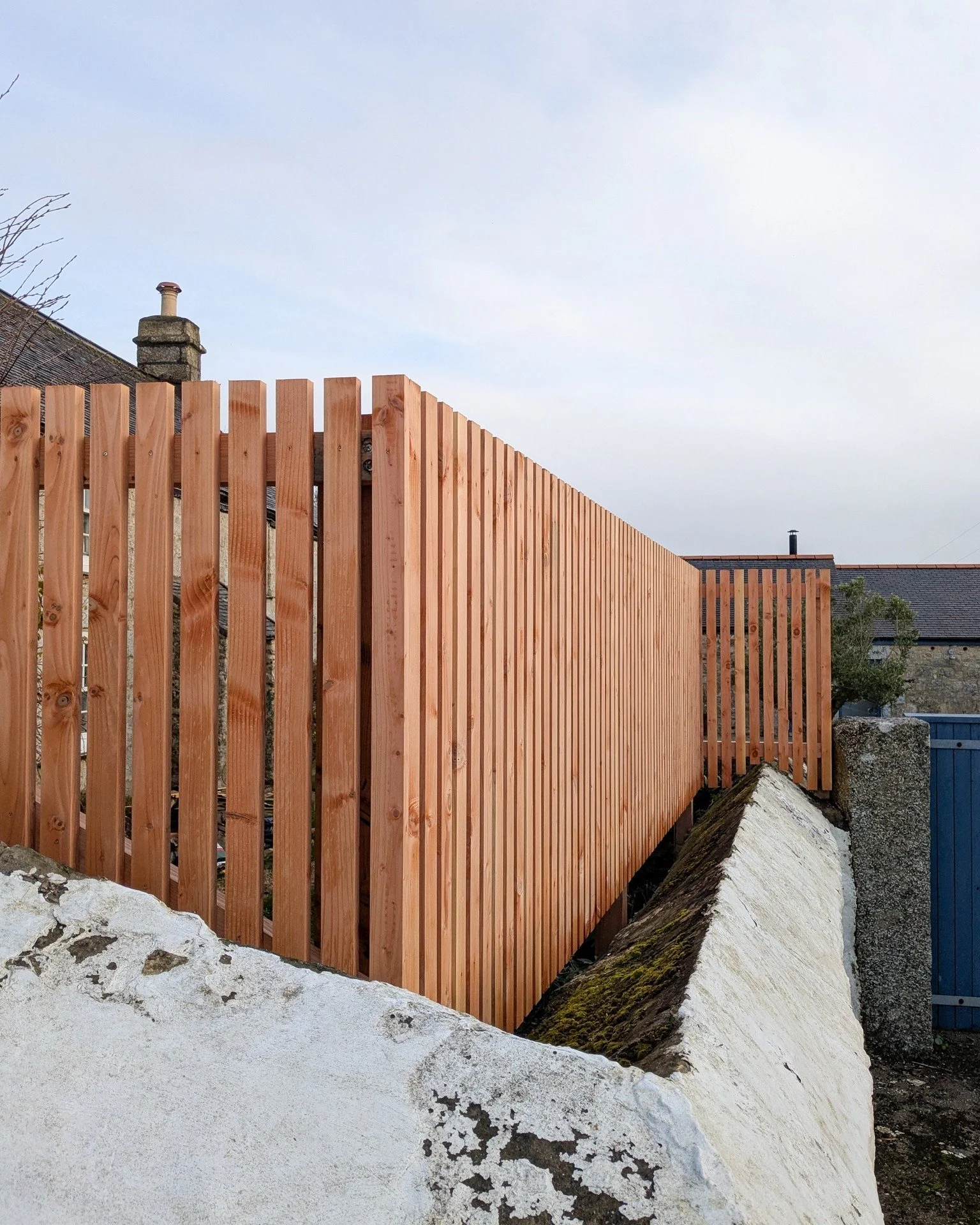 A vertical Douglas fir fence that significantly enhances privacy for the client. It sits atop the original granite wall, creating a seamless transition between the two structures. Replacing the old, weathered painted brown fence, the new design not o
