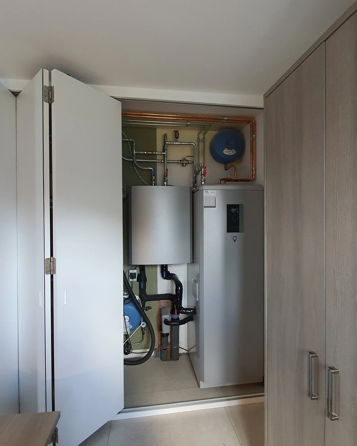 Open cabinet door revealing a water heater, pipes, and a water softener system inside a utility closet.
