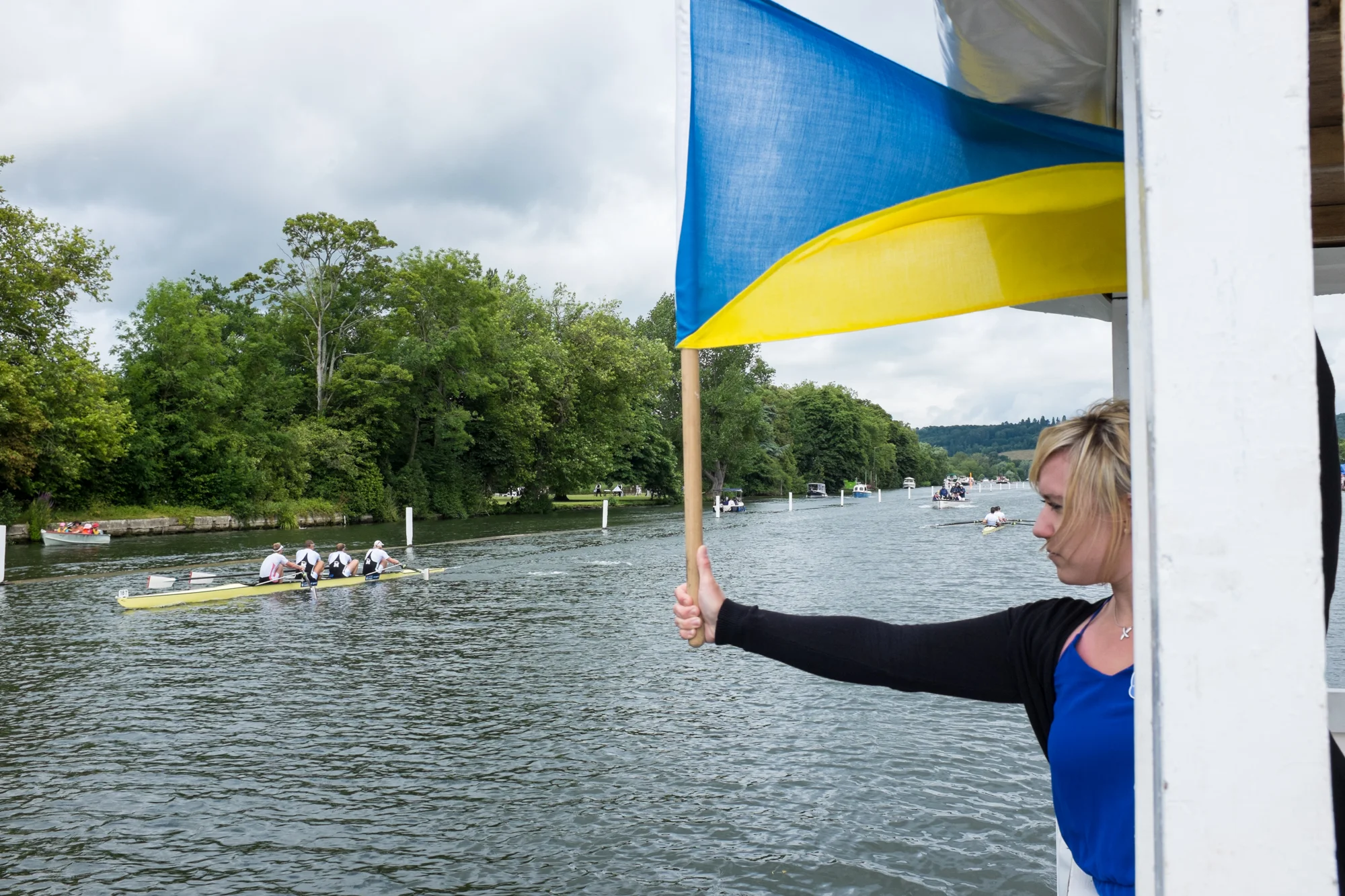 A signaller at Henley Royal Regatta drops a timing flag during a race as the leading crew passes the 1-mile point. A timekeeper on the umpire's launch following will make a note of the split time, and announce it to the crowds in the grandstands.