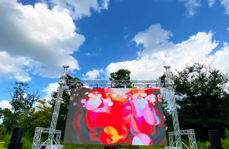 Outdoor LED wall installation on a grassy field, complete with scaffold support and audio gear — ideal for festivals, movie nights, or public events.