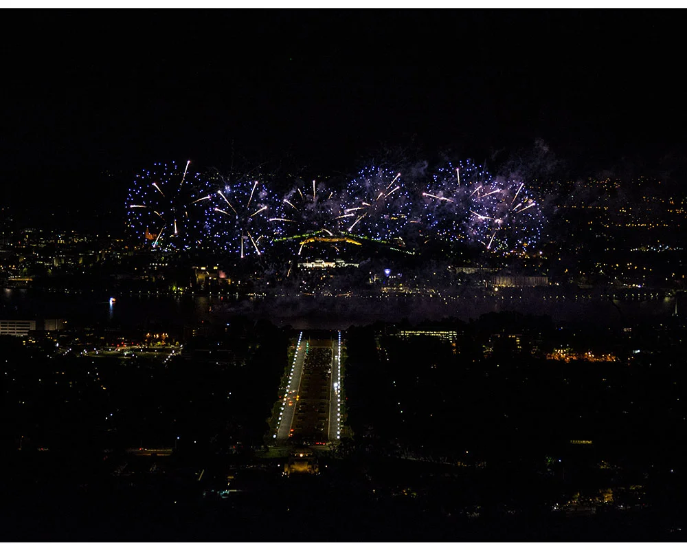 Fireworks display lighting up the night sky over a city skyline reflected on a body of water. Canberra Skyfire event.