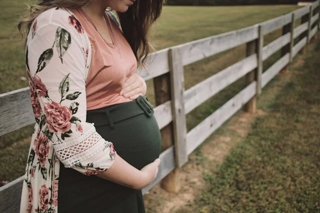 a pregnant woman by a fence holding her stomach