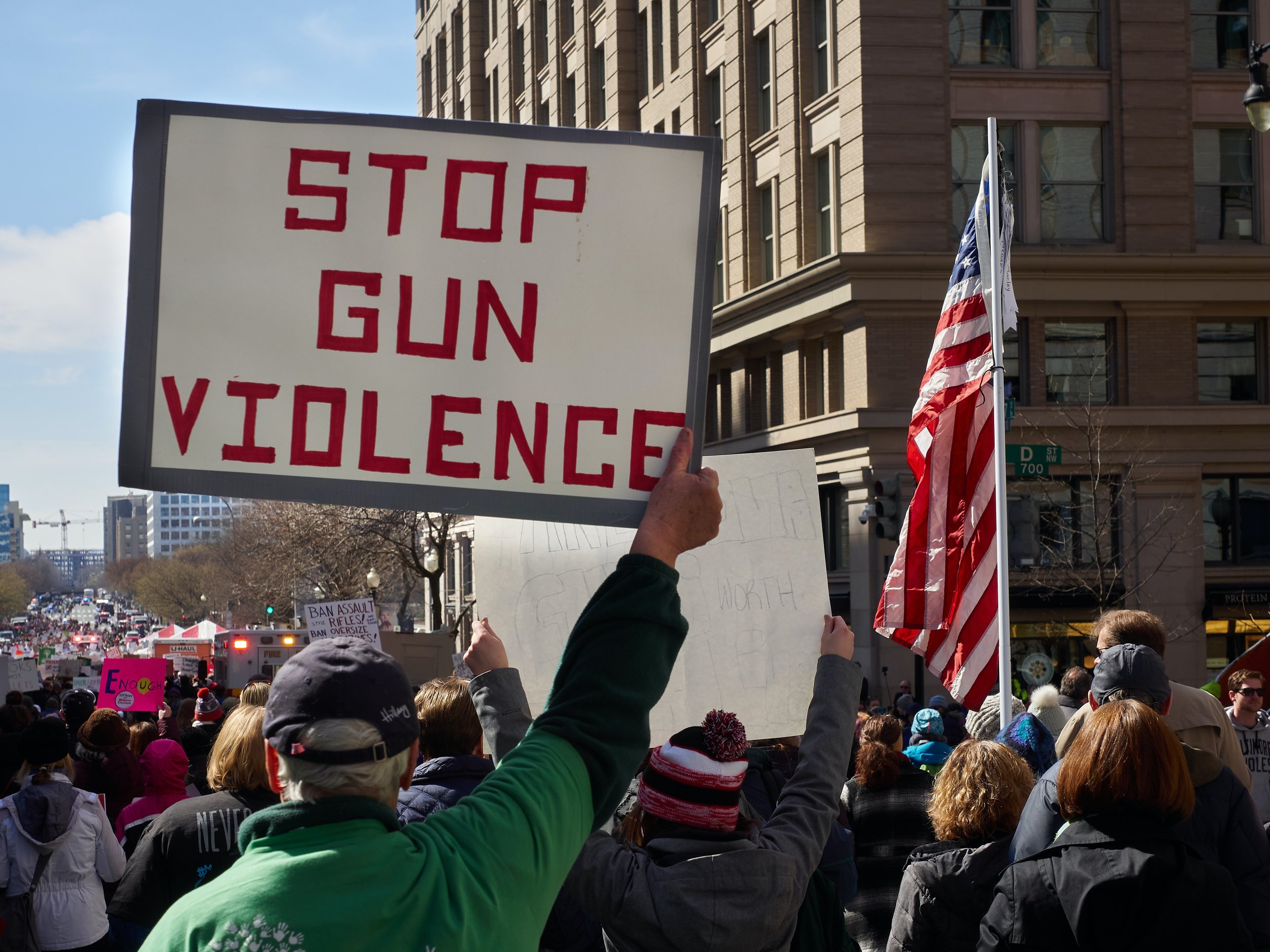 Image of people calling for an end to gun violence. One man holds up a sign that says "Stop Gun Violence"