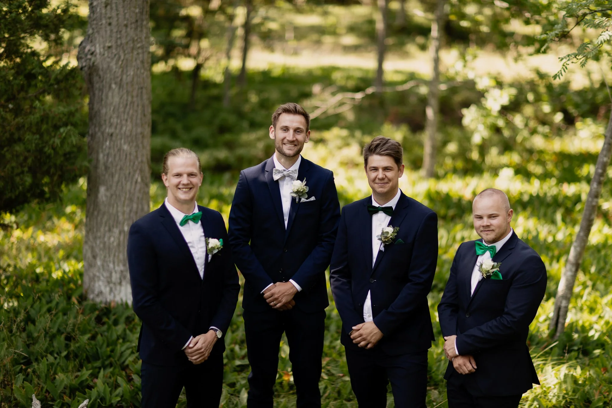 Brudgum med Marsalker står tillsammans utomhus bland träd och grönska, alla är formellt klädda med kavaj och fluga, och två av dem har blommor på kavajen. De ler mot kameran ute i gränsö slott.