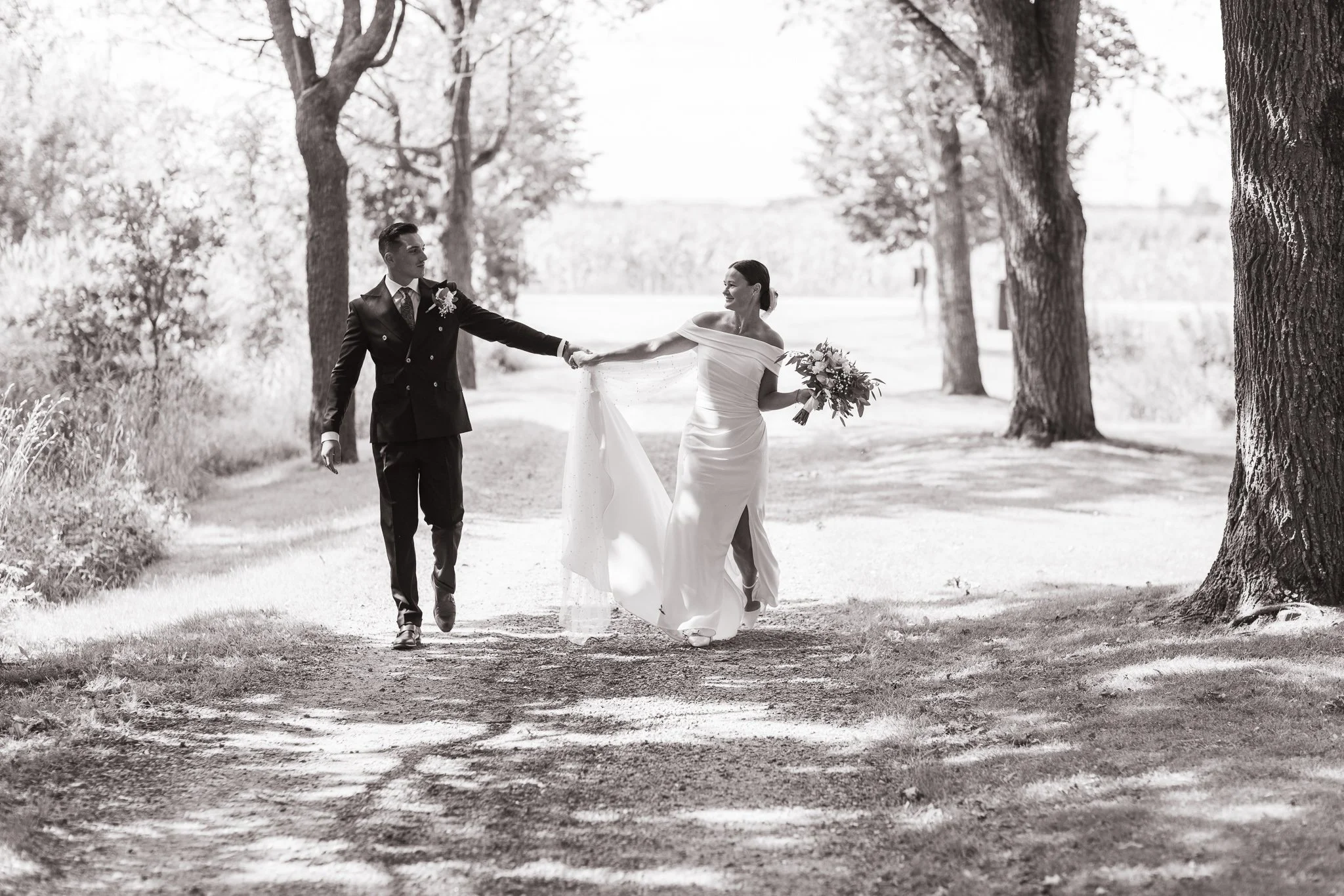 Brudpar håller handen när de går i en alle under sin bröllopsfotografering i Olais Lada. Bröllopsfotograf i Linköping Östergötland
