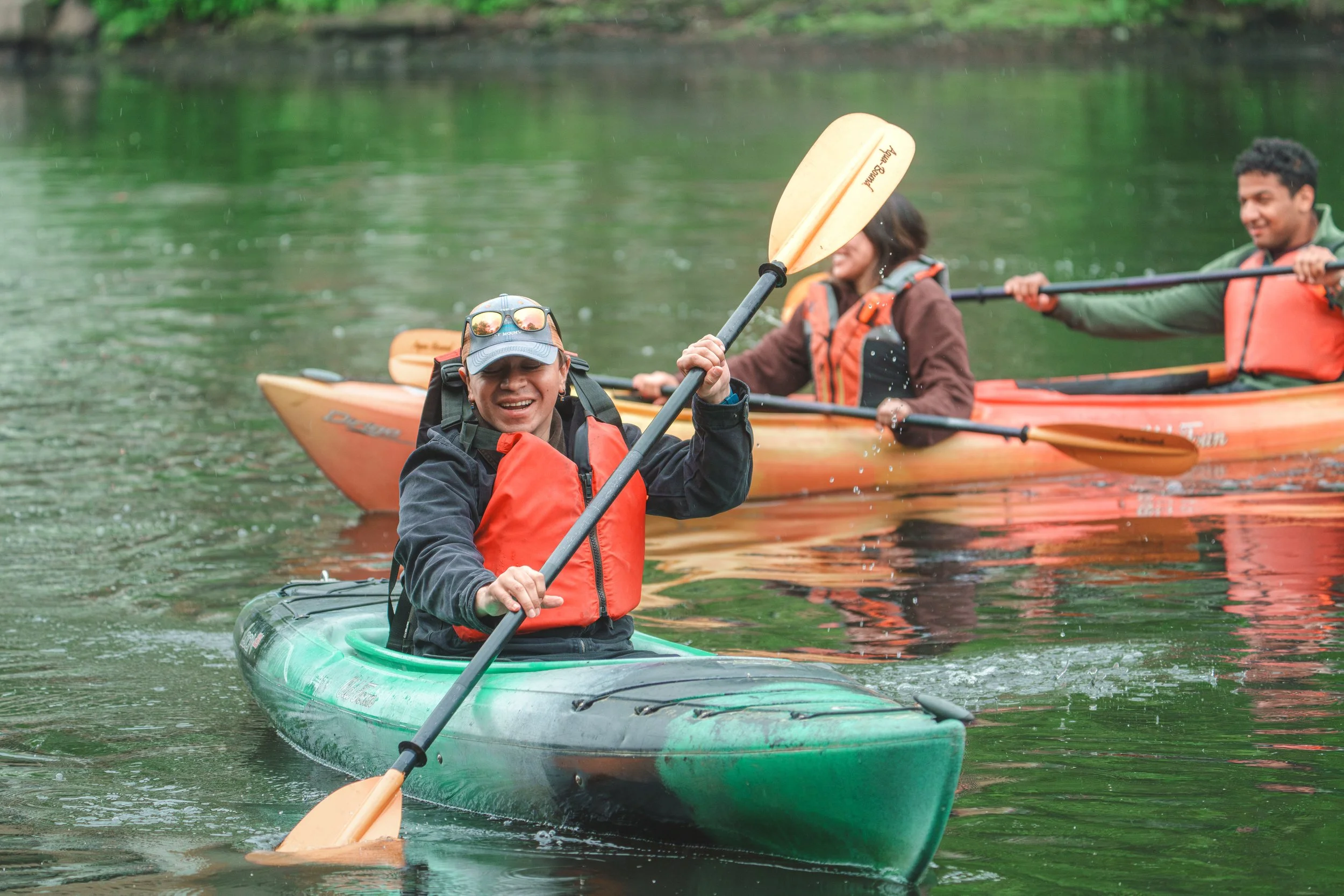 Three people kayak on the Mystic River.