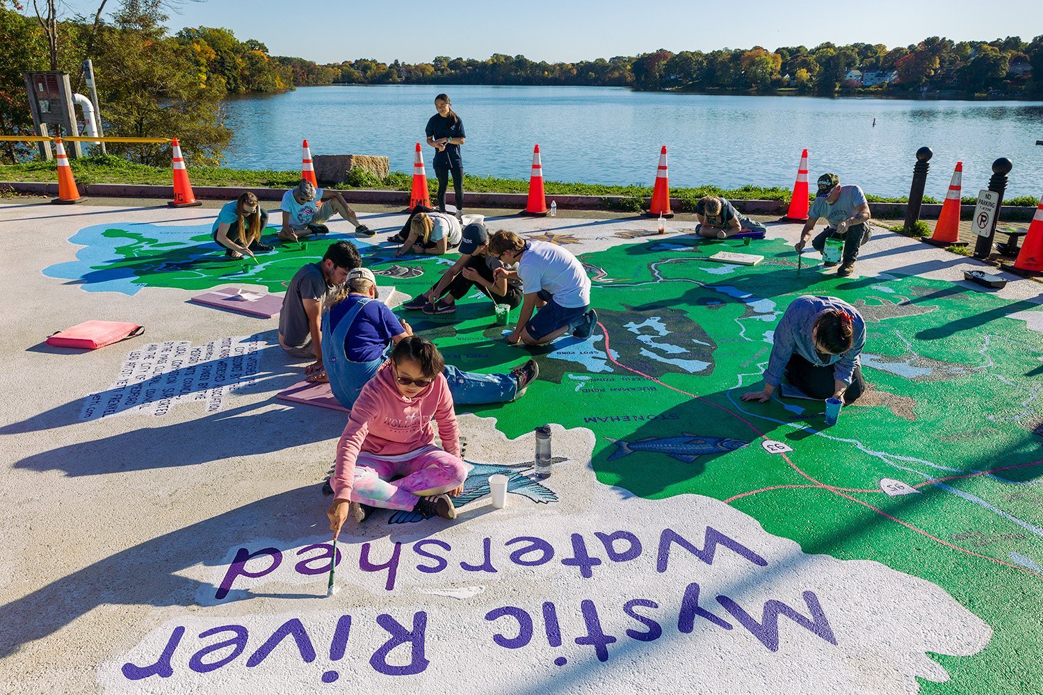  10.15.2022 | Volunteers help to refresh the  Mystic River watershed mural  at the Mystic Lakes Dam alongside the original artist Yetti Frenkel. Credit: David Mussina 