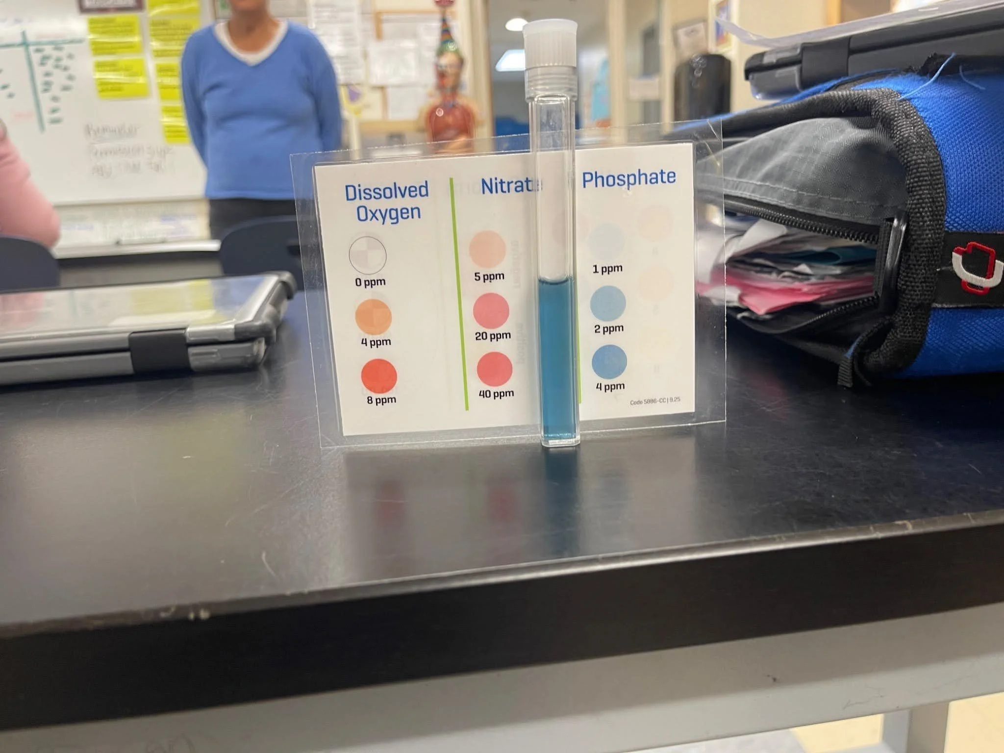 A test tube with blue liquid on a lab table in a classroom next to a diagram with a key that shows how to interpret what the color of the liquid means