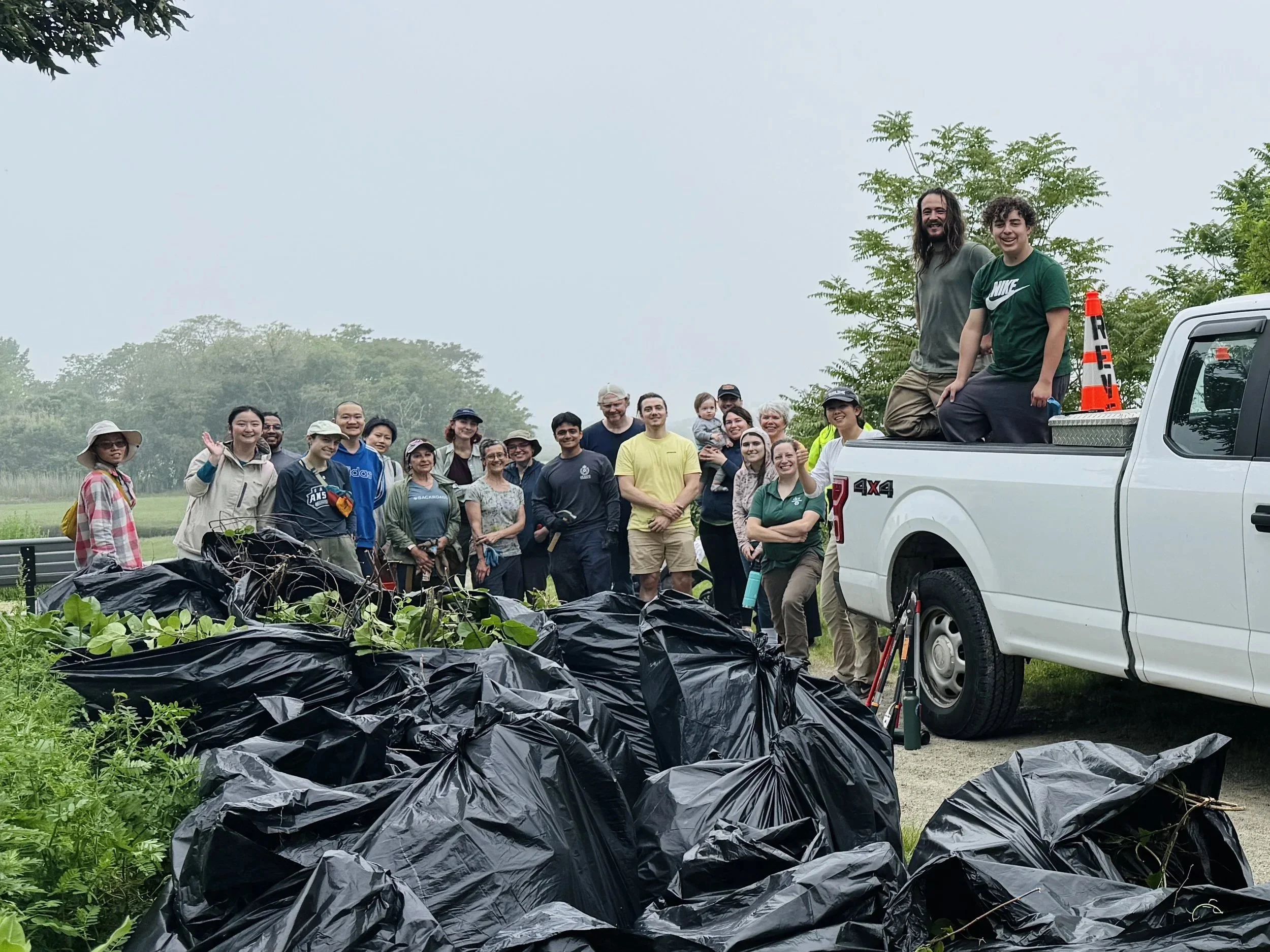 A group photo with bags of invasive plants and Belle Isle Marsh in the background.