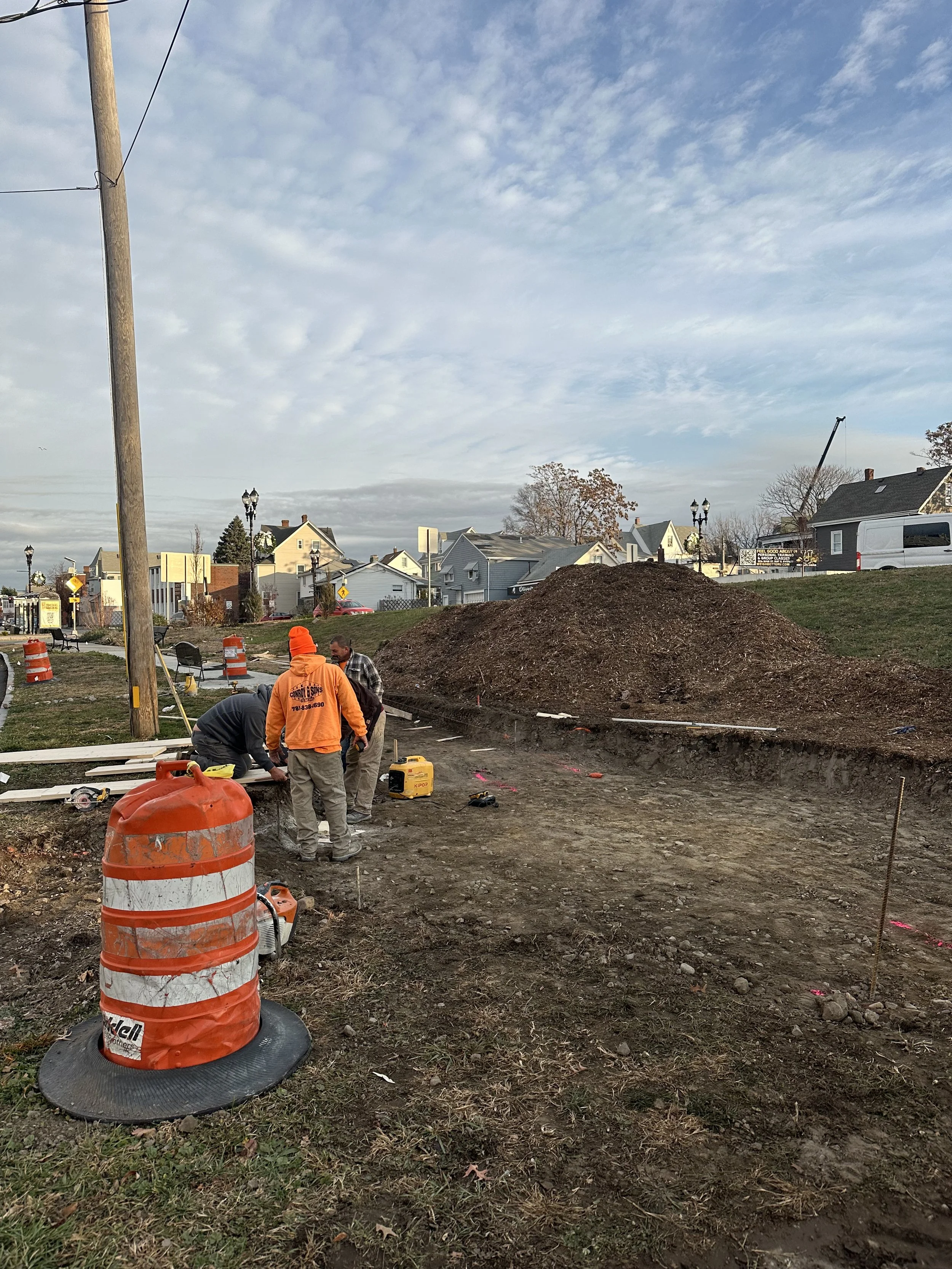 Construction workers prepare the site at Main Street Meadow with excavated soil and construction equipment visible.