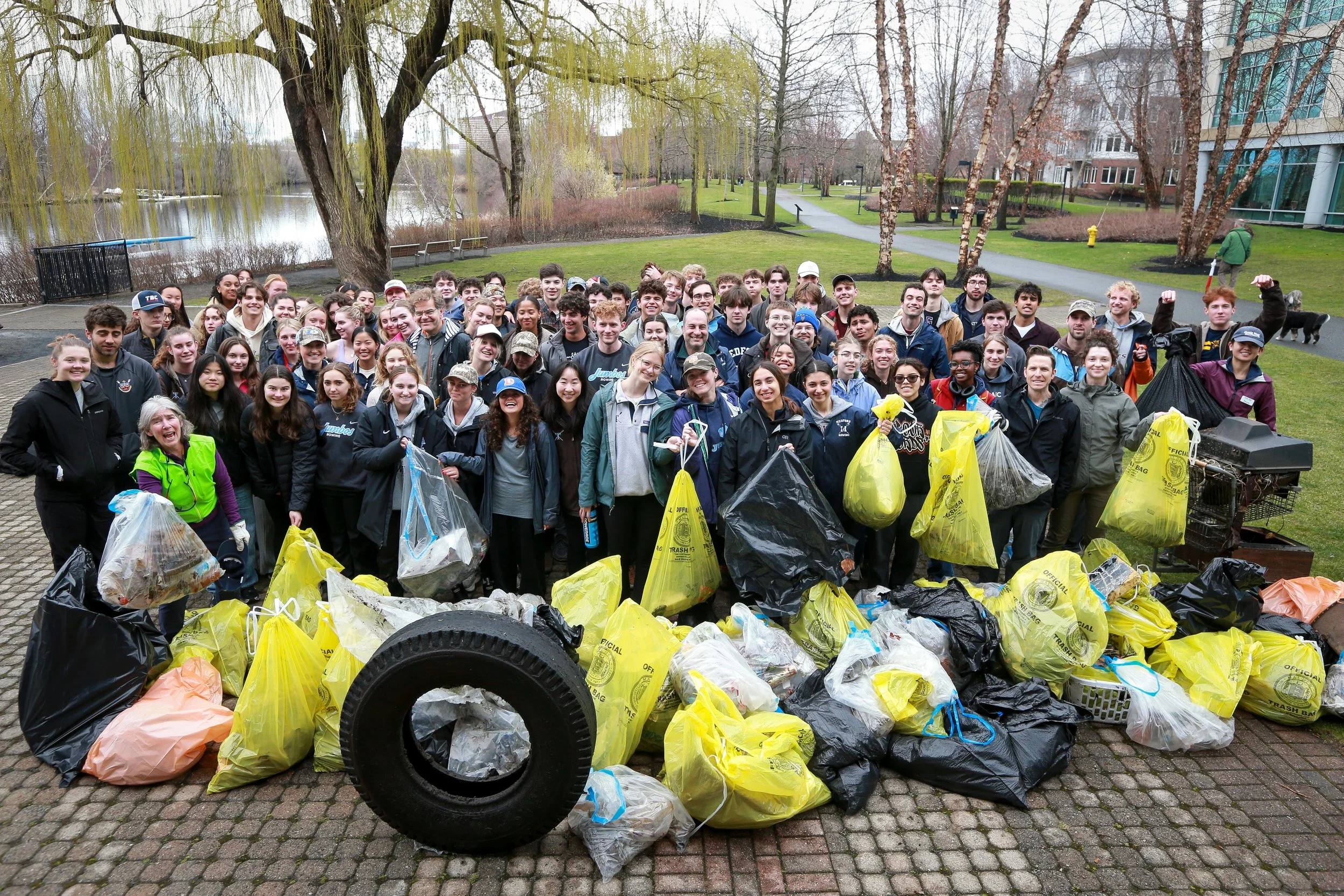 A large group photo of volunteers with their collection of trash bags and items at the Malden River.