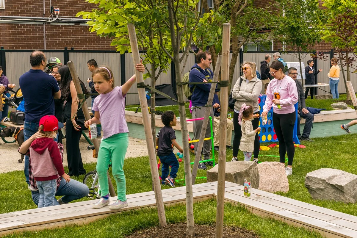 Children play on newly installed benches and grassy areas while parents watch.
