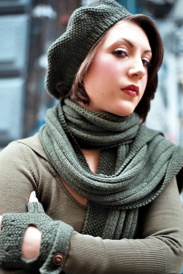 A young woman with short brown hair wearing a green knit beret, large green scarf, matching fingerless gloves, and a khaki sweater.