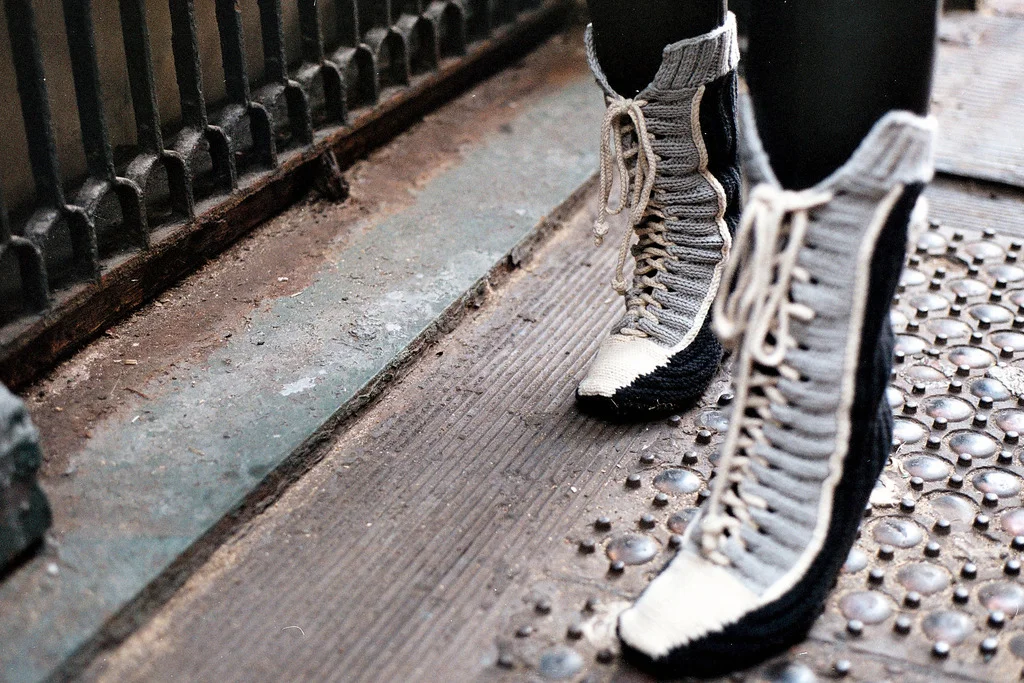 Person wearing high-top, knit grey and black sneakers standing on a wooden and metal platform.