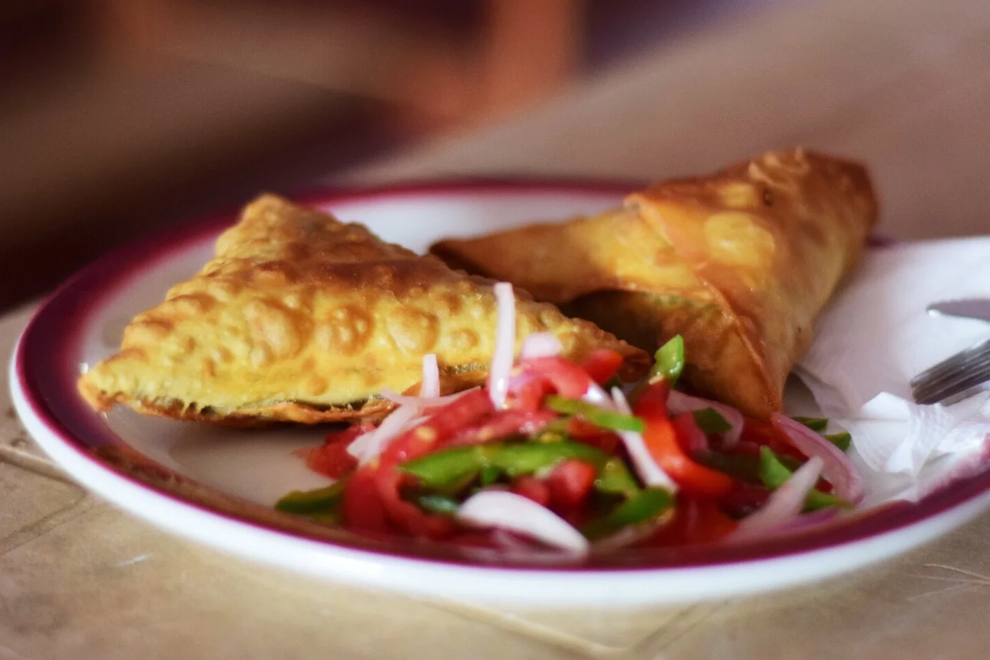Close-up of two samosas with a side of mixed vegetable salad on a white plate with red trim in Mbale, Uganda.