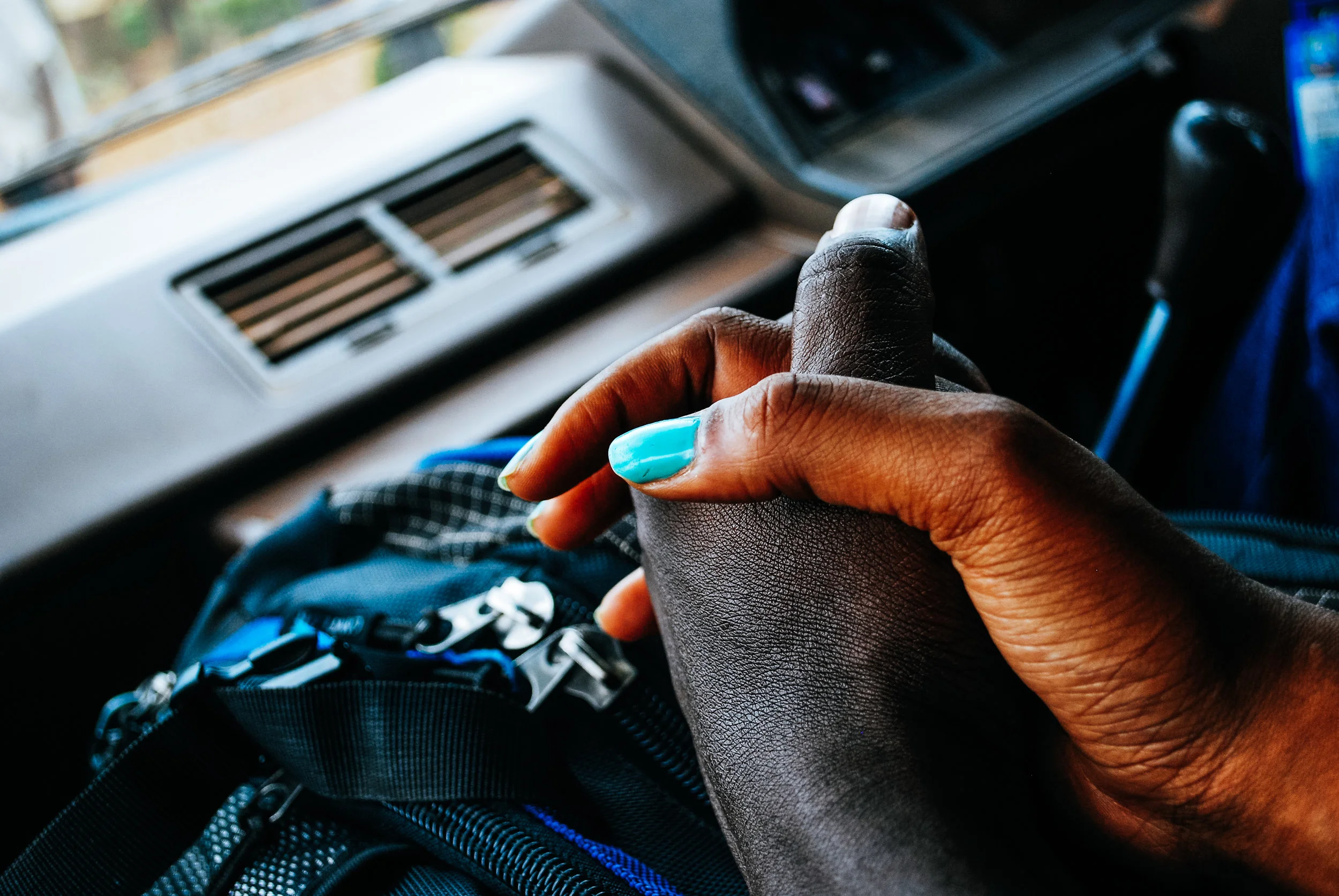 Close-up of a person's hand with blue painted nails, resting on a backpack in a vehicle in Uganda.