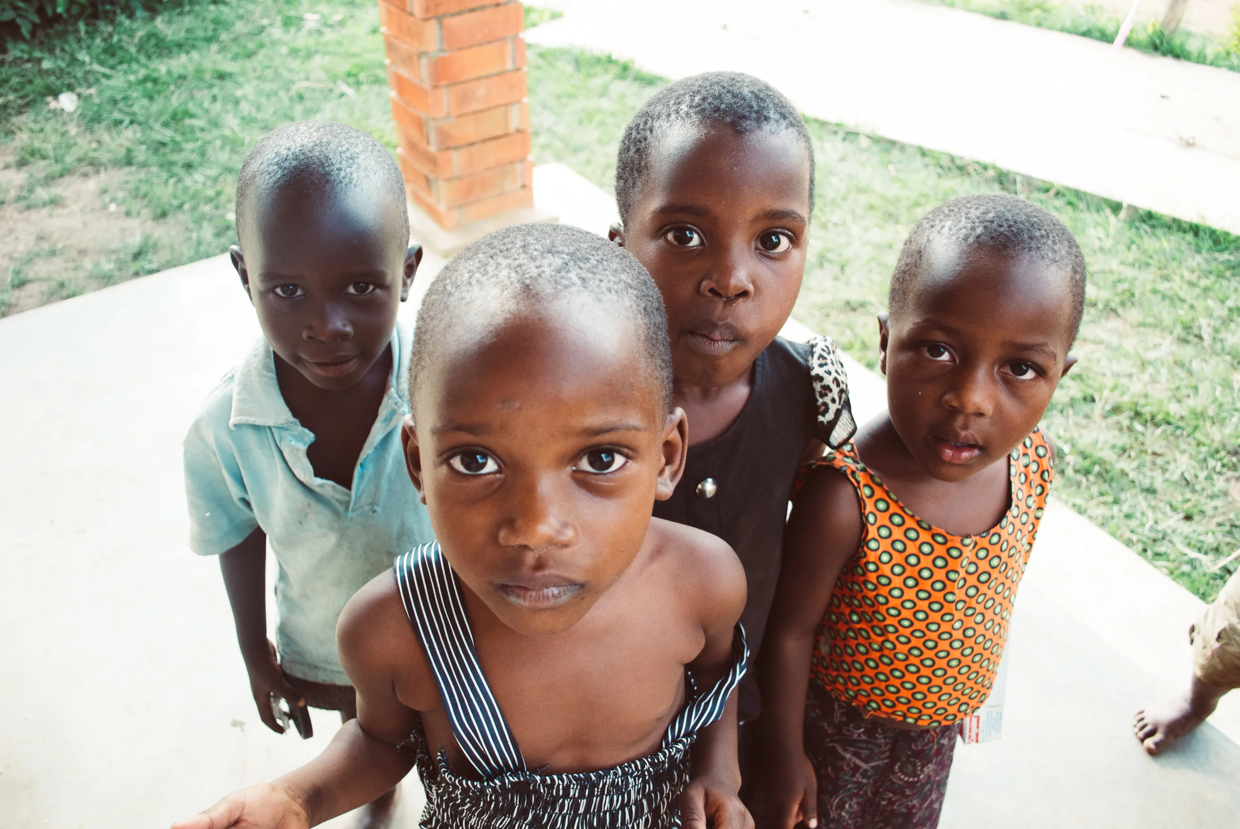 Four young children standing outdoors, looking up at the camera with curious expressions in Uganda.