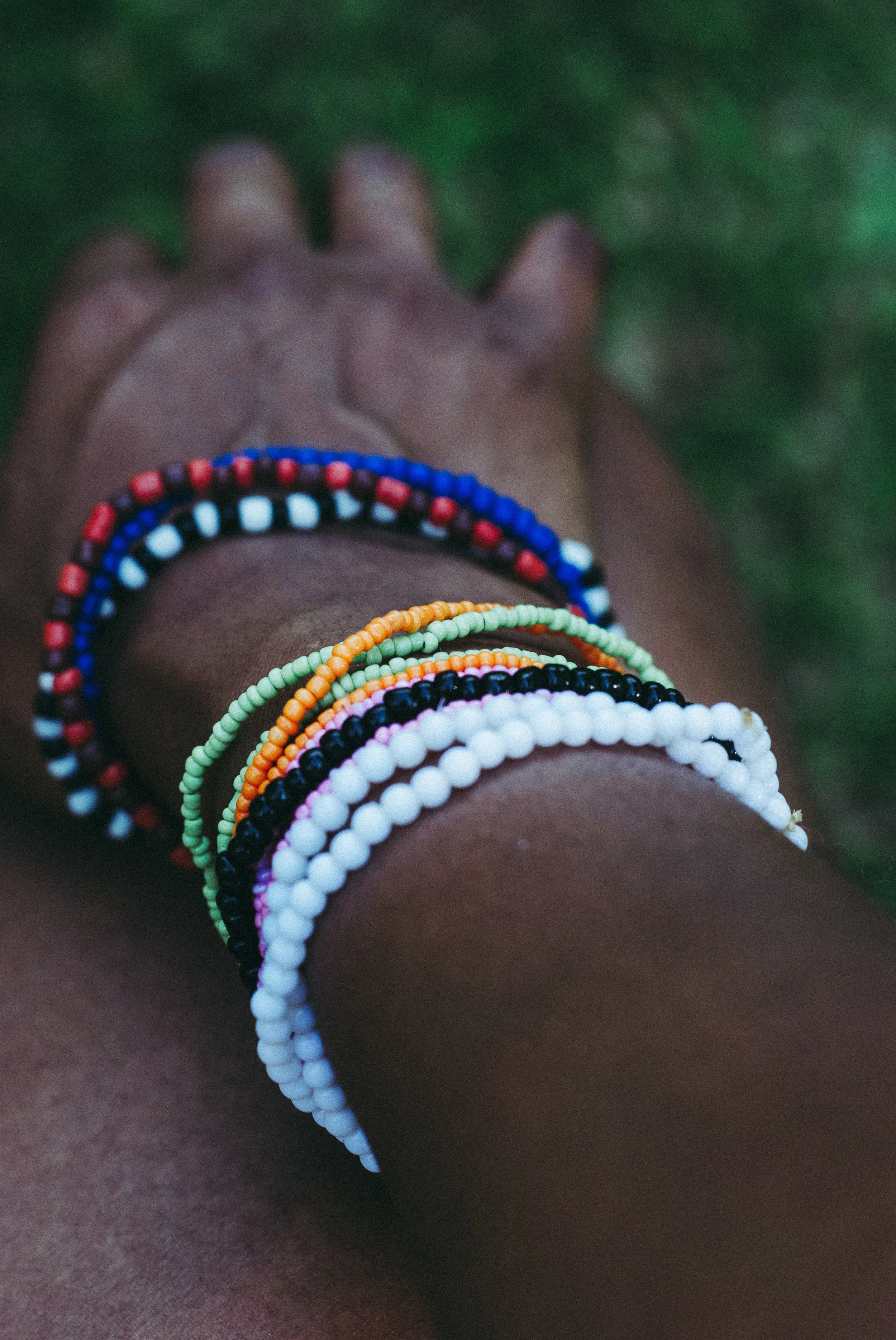 Close-up of a person's arm with five colorful beaded bracelets, with a blurred green outdoor background.