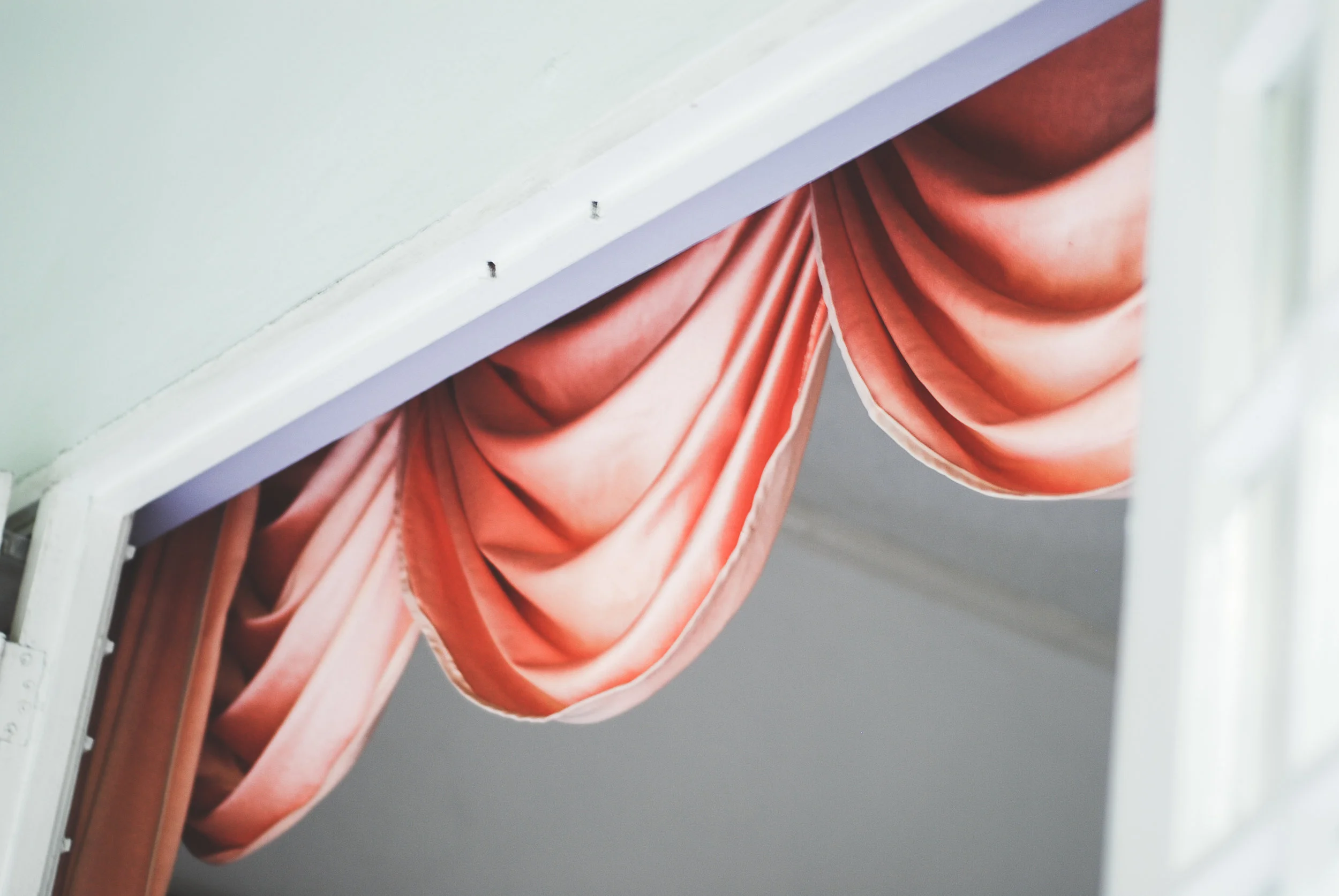 Pink velvet curtains hanging from a window with a white frame, partially open.