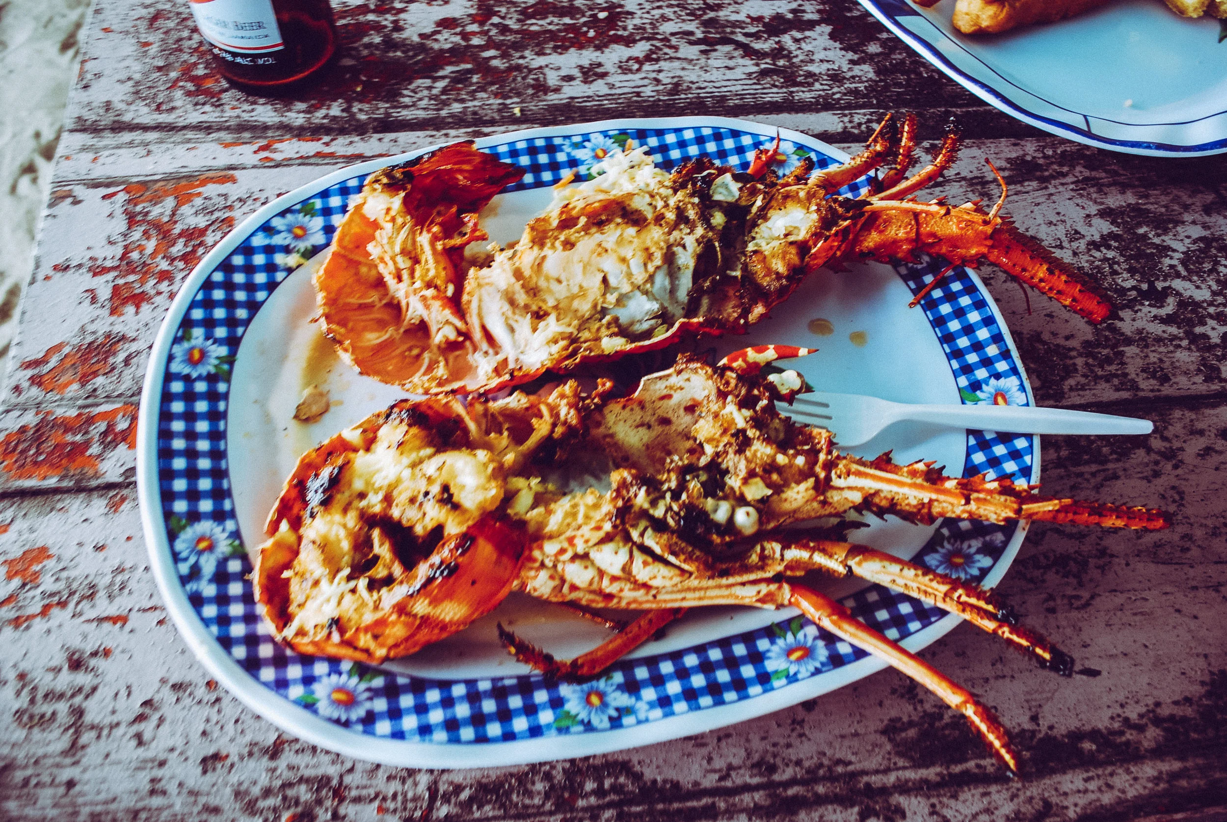 A plate with cooked lobster on a checkered-patterned plate on a rustic wooden table on Hellshire Beach in Kingston, Jamaica.