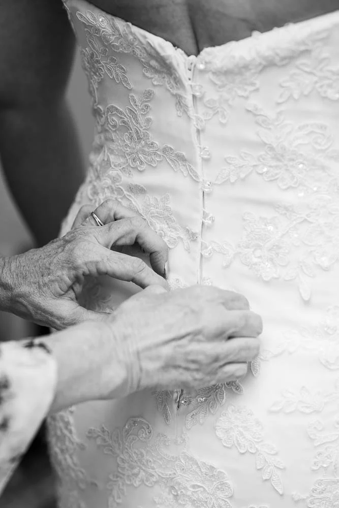 A black and white portrait of a mother helping her daughter with her dress during a St. Louis wedding. 
