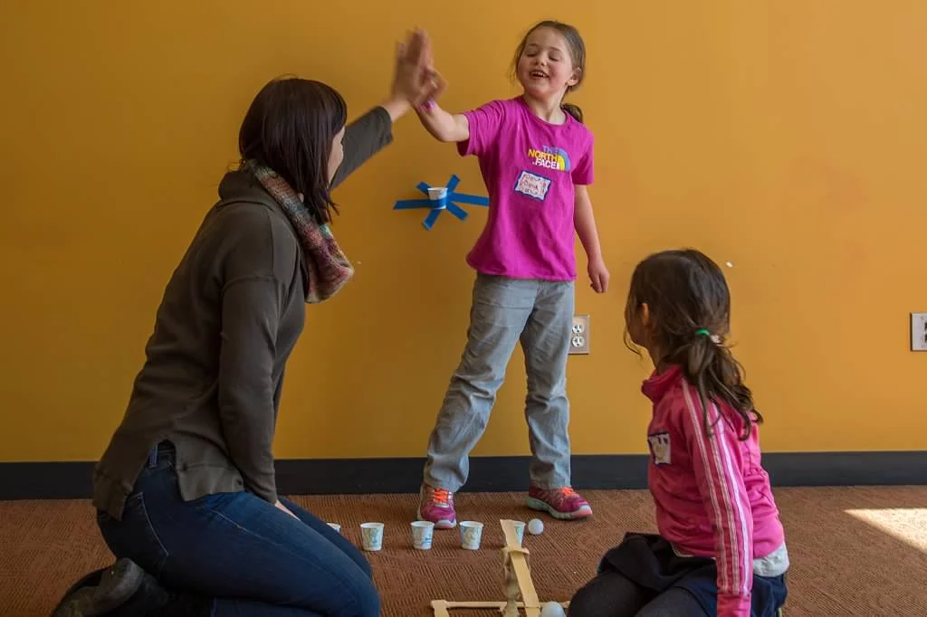 A mom and daughter slap-five after getting their ping pong ball launcher to work at our STEM program Build Bridges! Photo by Diane Hammer
