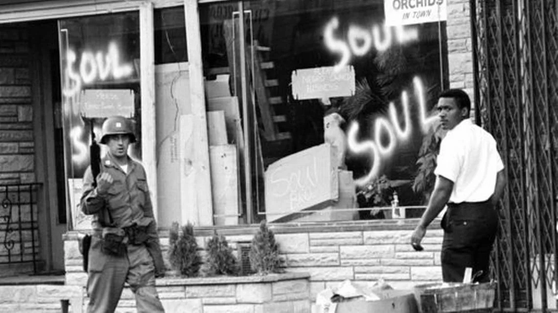 FILE - In this July 15, 1967 file photo a National Guard officer passes the smashed window of a black-owned flower shop in riot-torn Newark, N.J. The last surviving member of the Kerner Commission says he remains haunted that the panel's recommendations on US race relation and poverty were never adopted, but he is hopeful they will be one day. Former U.S. Sen. Fred Harris says 50 years after working on a report to examine the causes of the late 1960s race riots he strongly feels that poverty and structural racism still enflames racial tensions even as the United States becomes more diverse. AP Photo,File)