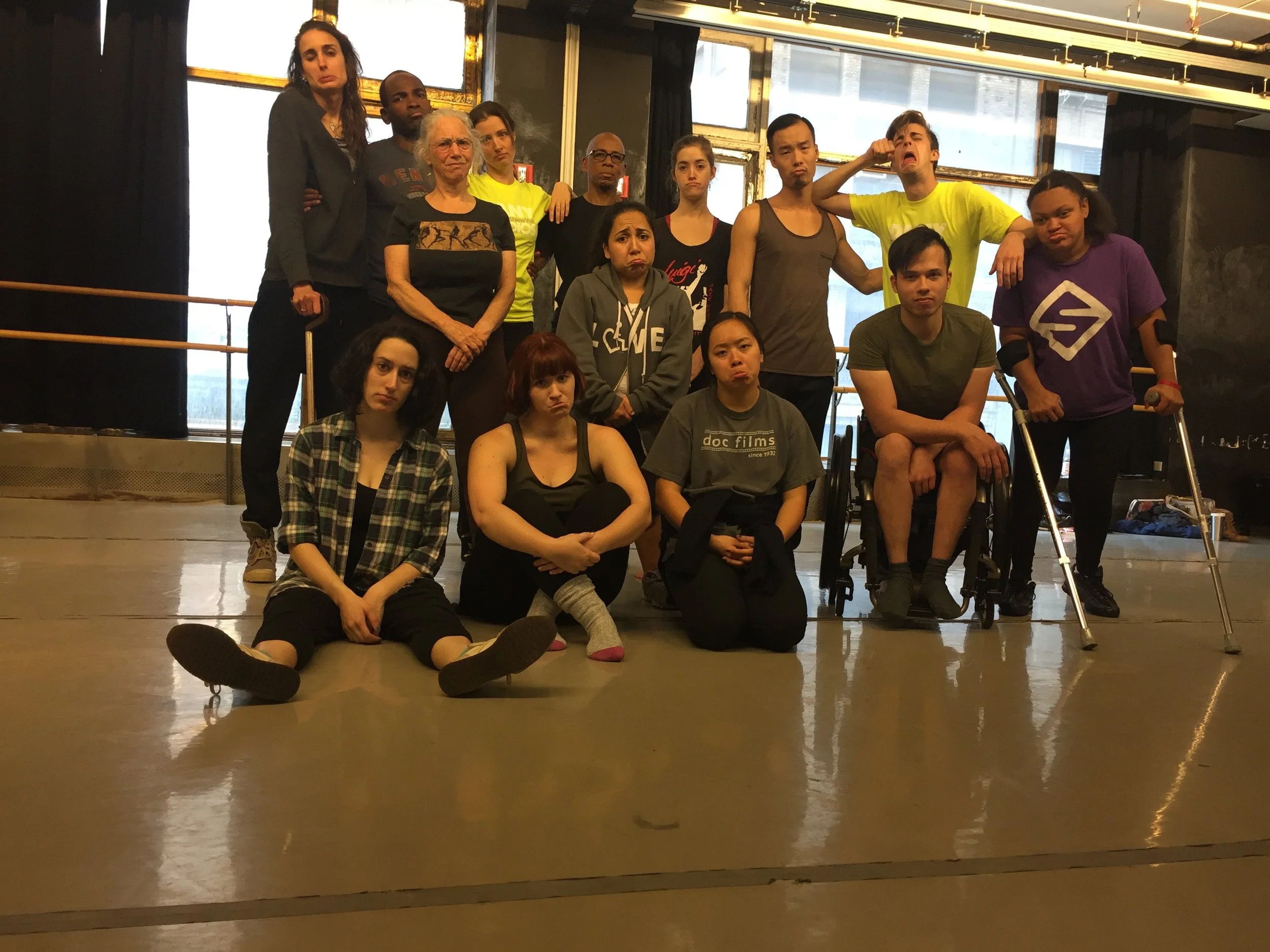 Large group of dancers in a rehearsal studio making sad faces at the camera.