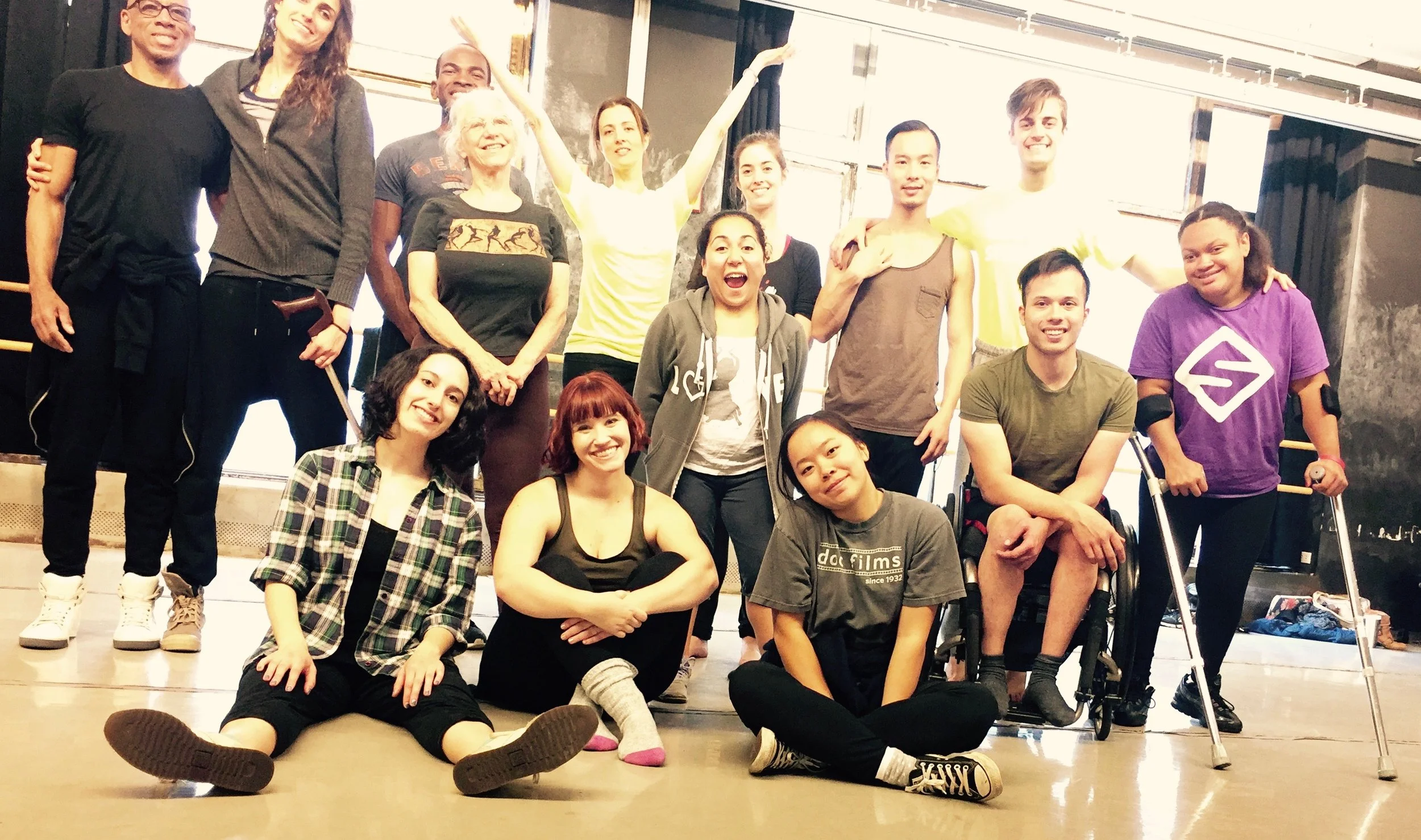 Large group of dancers smiling at the camera in rehearsal.