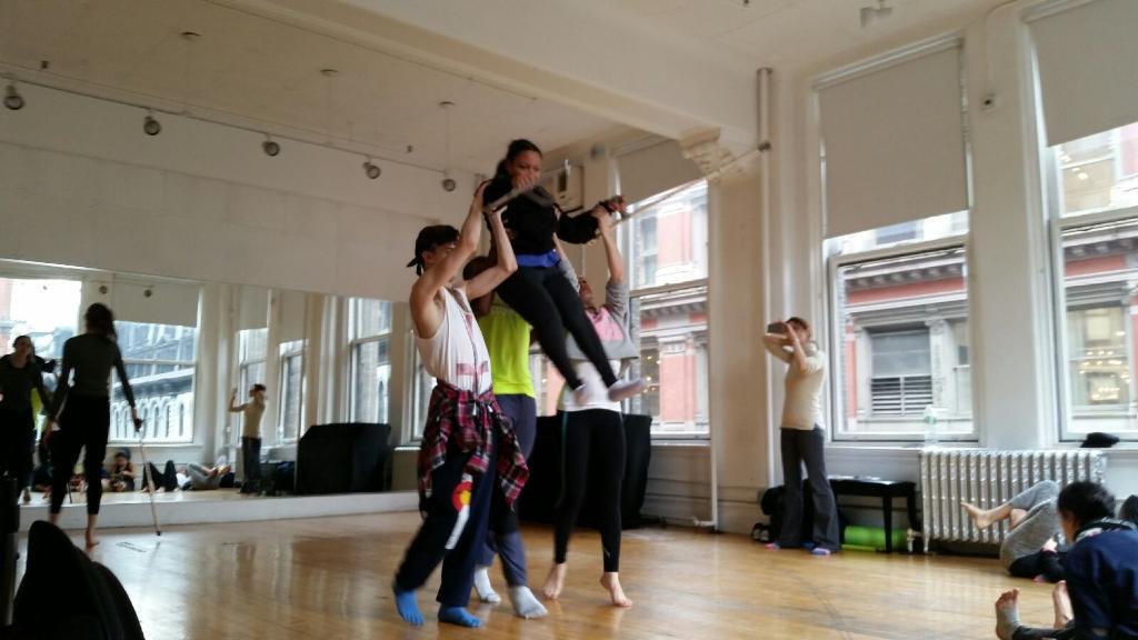 Dancer Stephanie being lifted up high by two other dancers with her arms and crutches extended out.