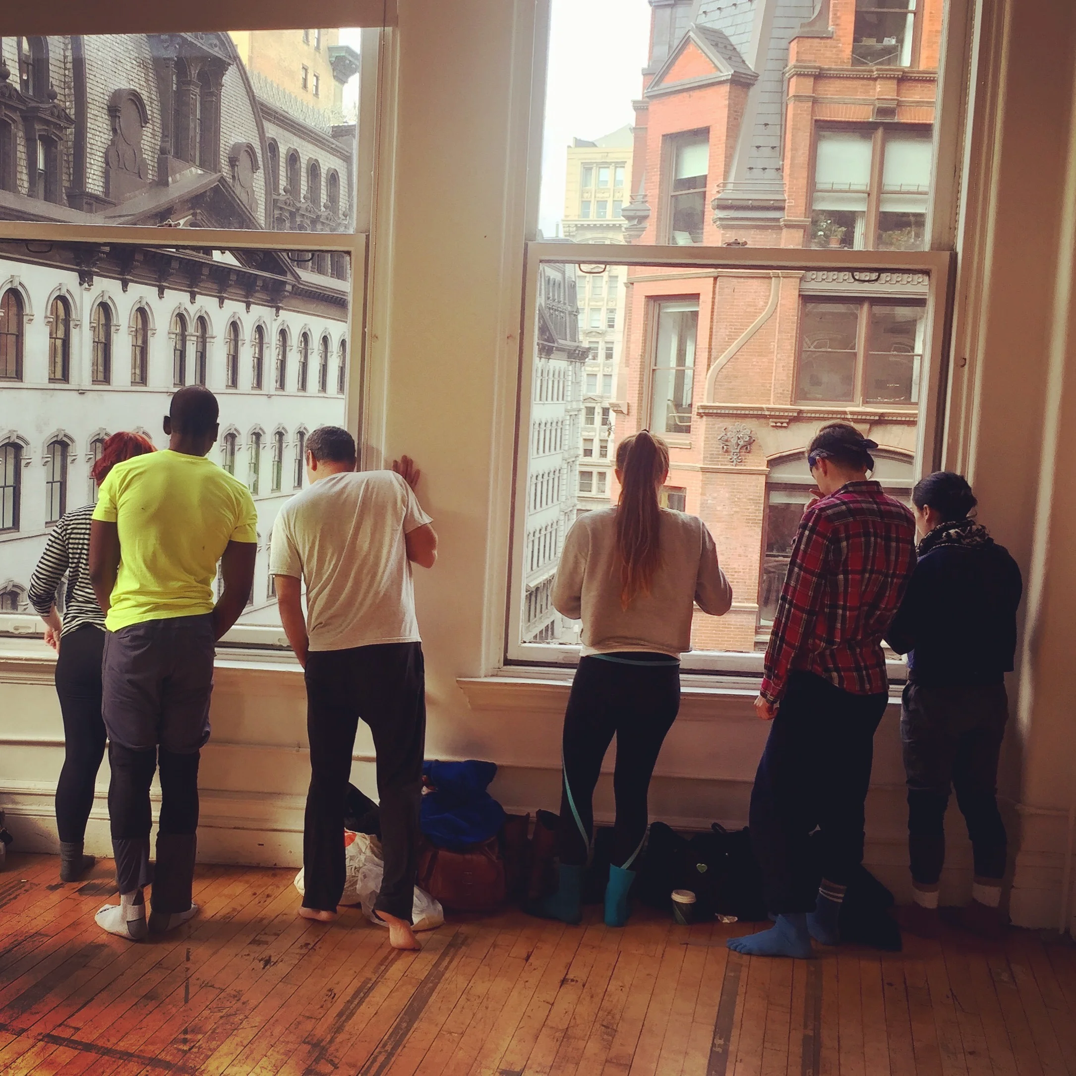 Six male and female dancers looking out the window of a downtown dance studio.