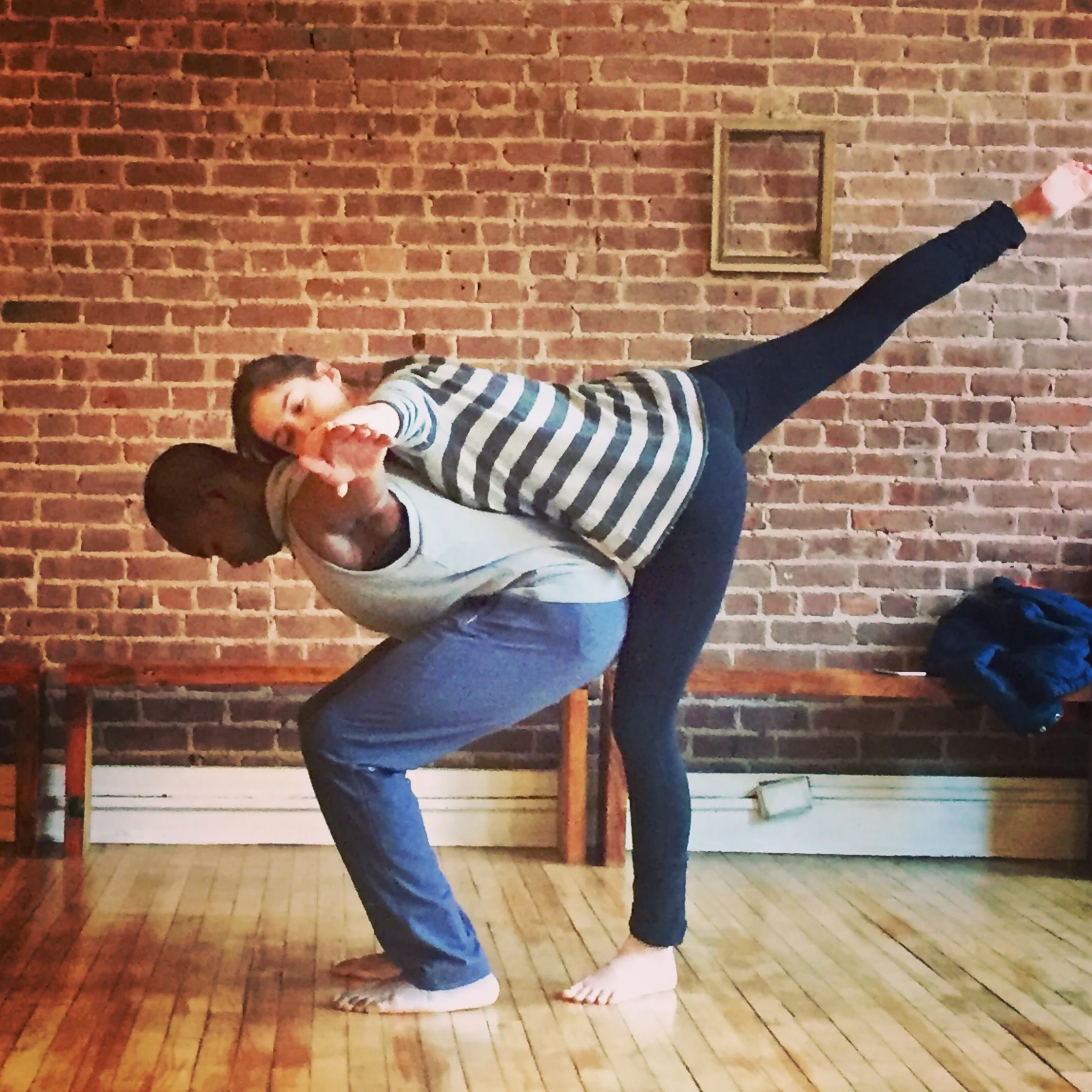 Katie leaning on John’s back with leg extended behind her while John folds forward in rehearsal.