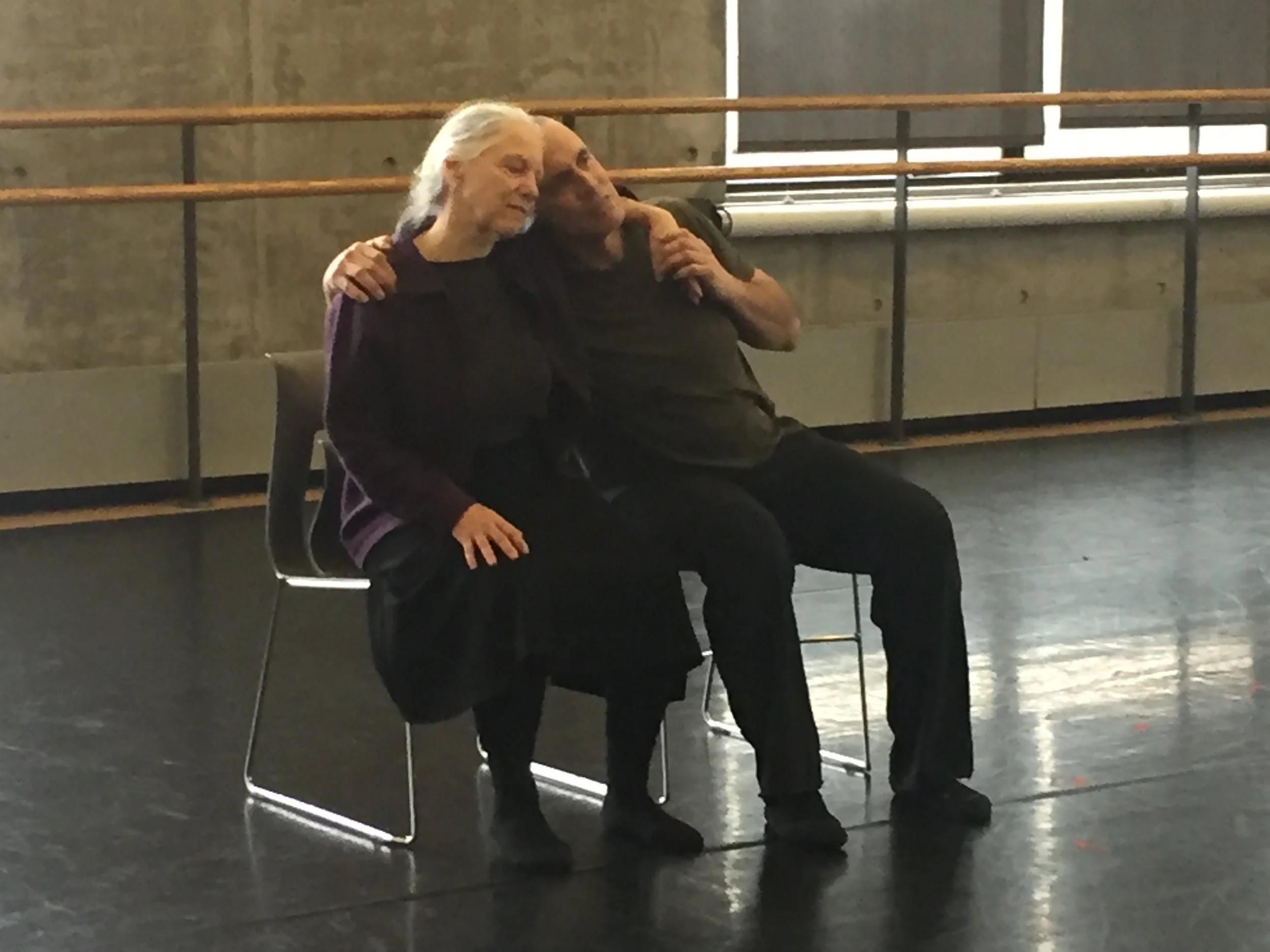 Sara and Tom sitting on chairs with arms wrapped around each other in rehearsal.