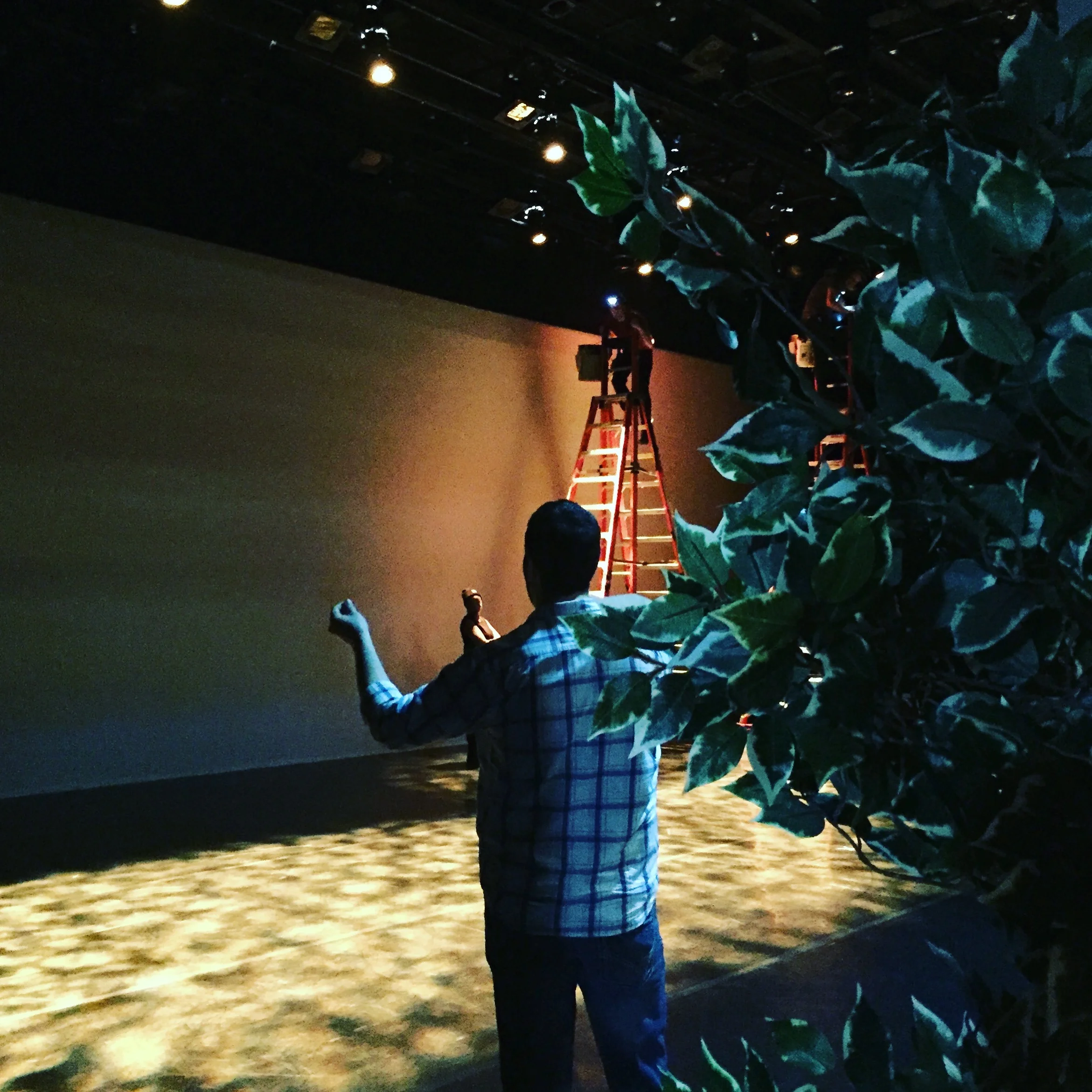 Lighting Designer Michael giving instructions to team focusing lights on ladders on stage at theater.