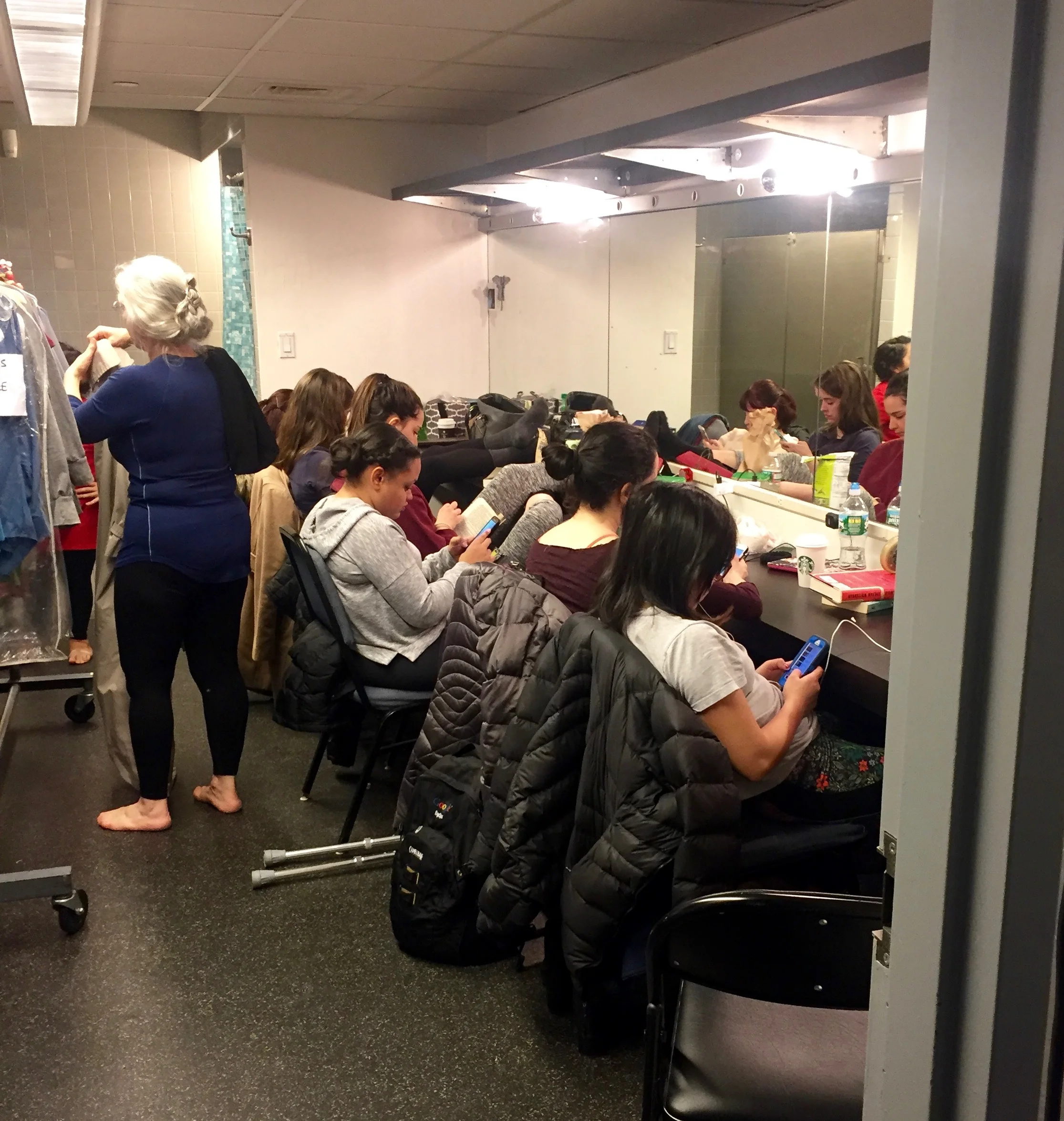 Dancers in the women’s dressing room talking, using their phones, and getting ready.
