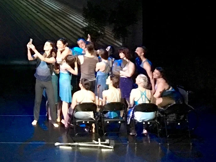 Dancers dressed in blue and teal costumes portraying a scene on a NYC subway on stage.