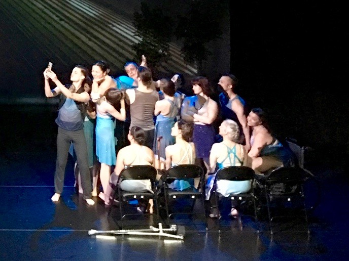 Dancers dressed in blue and teal costumes portraying a scene on a NYC subway on stage.