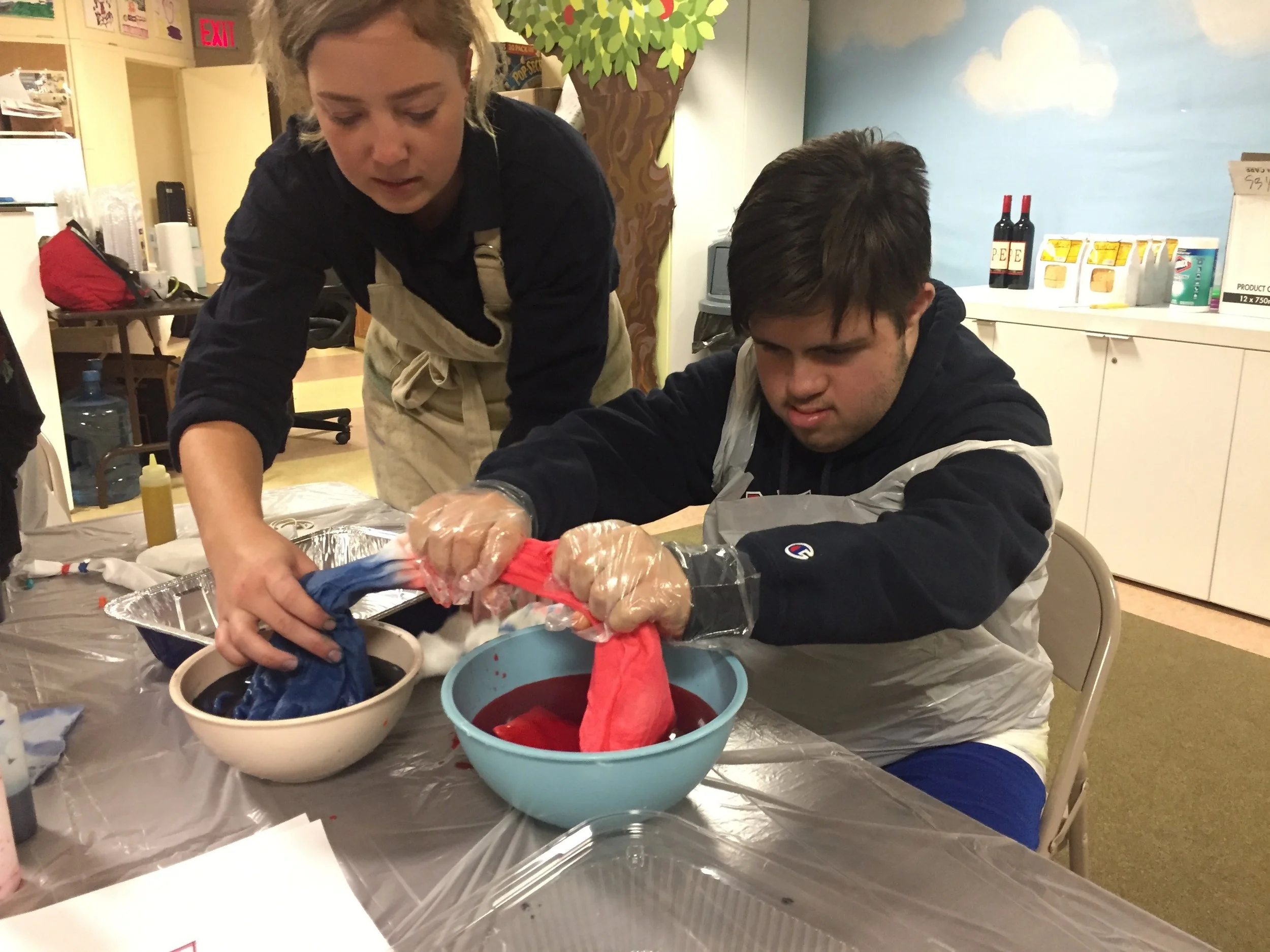 Costume Designer Stacy Jansen teaching apprentice John how to dye fabric. John is dying white fabric blue and red in large bowls.