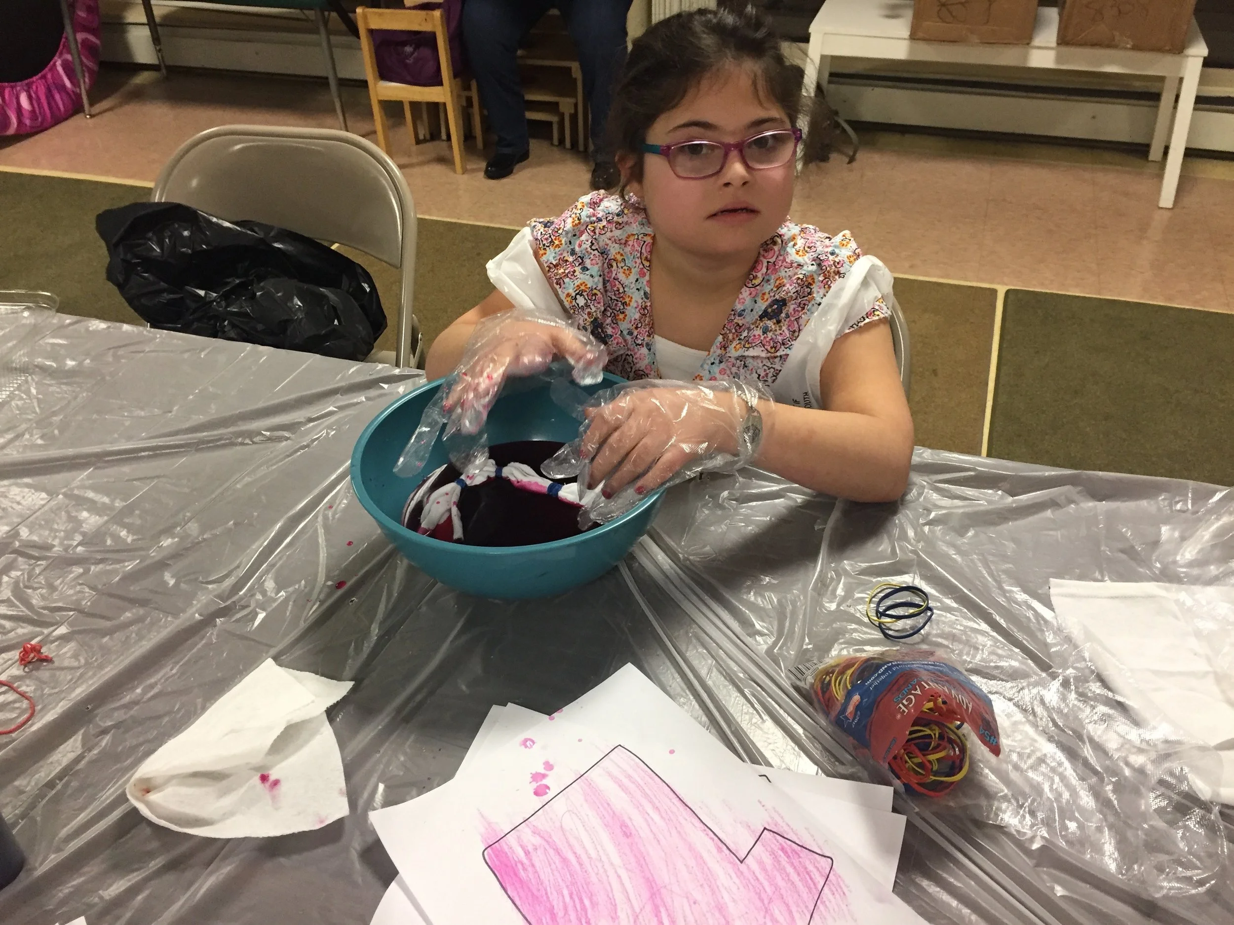 The apprentice Sofia dying white fabric in a large bowl while wearing gloves.