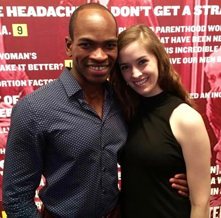 Dancers Katie Wilson and John Fiscian standing next to each other with arms around each other smiling in front of a red background.