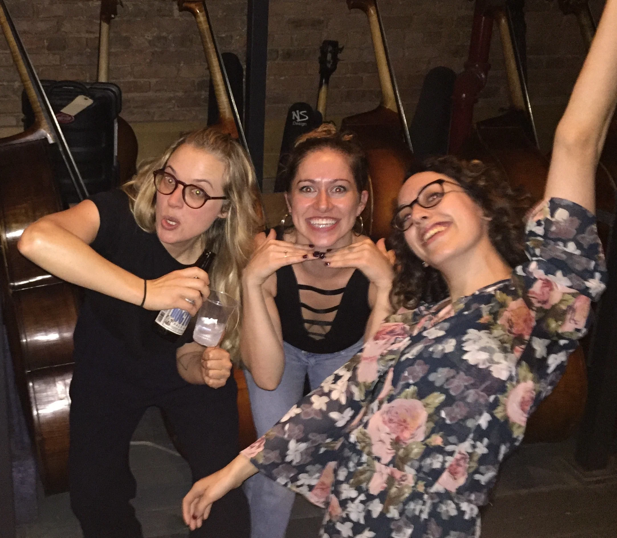 Singer/songwriter Misty Boyce and dancers Madeline Charles and Juliana Garber making funny poses and faces at the camera in front of a row of cellos.