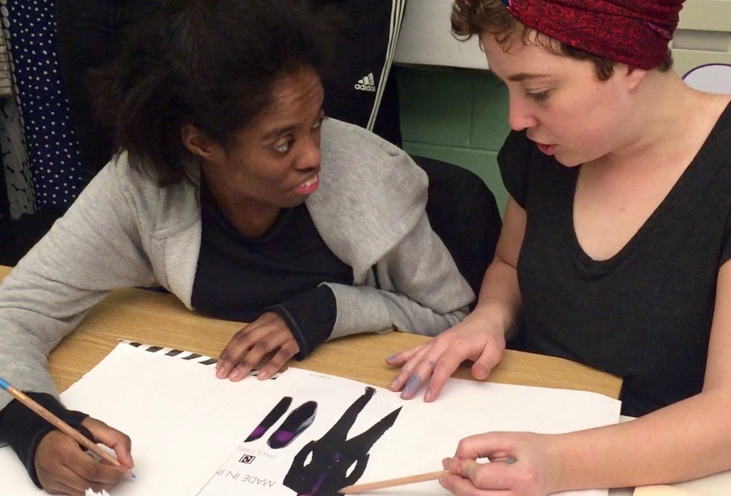 Costume Designer Stacy Jansen teaching an apprentice while they both draw costume ideas on white paper.