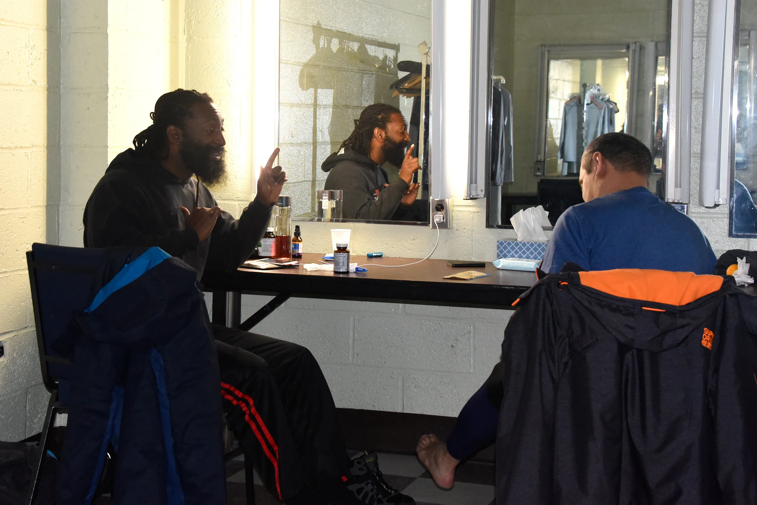 Dancers Samuel Caraballo and Antoine Hunter seated at the mirrors in the dressing room having a conversation in American Sign Language.