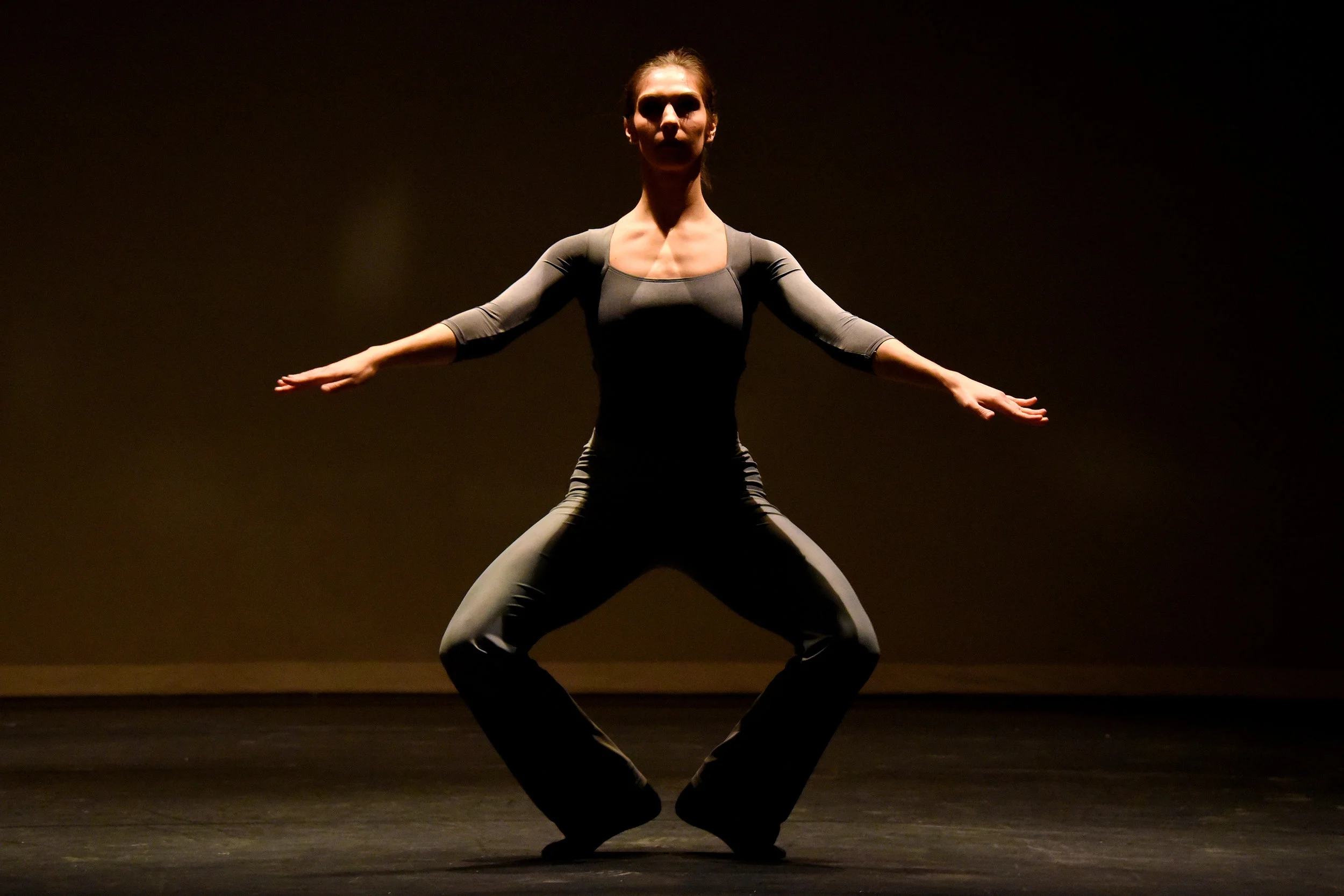 Dancer Meagan Kolakowski warming up in costume on a dimly lit stage and practicing a grand plié.